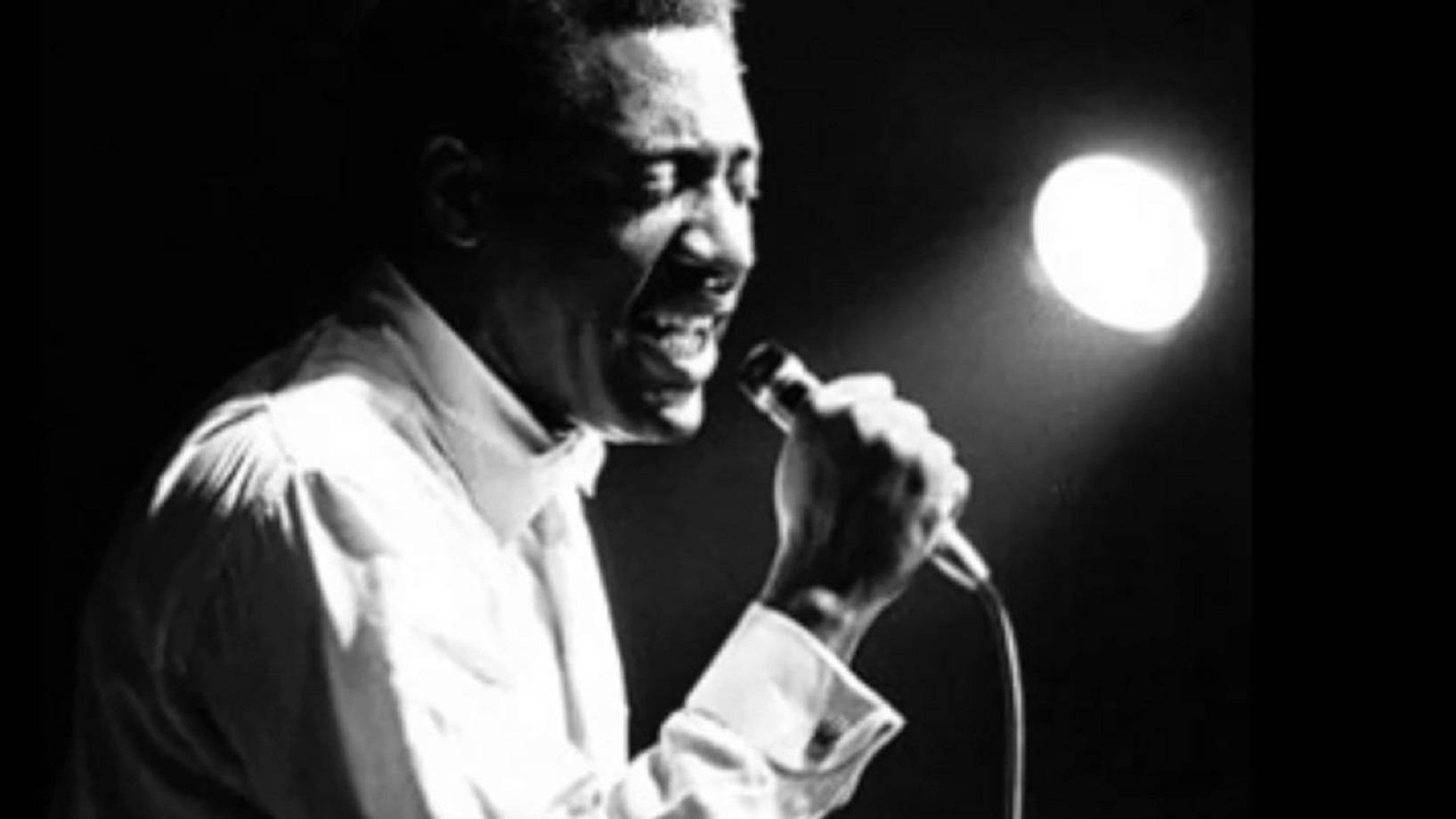 Singer 桌布 壁紙 — 一個黑白肖像，一個微笑的男人在黑暗舞台上的單一聚光燈下對著麥克風唱歌。