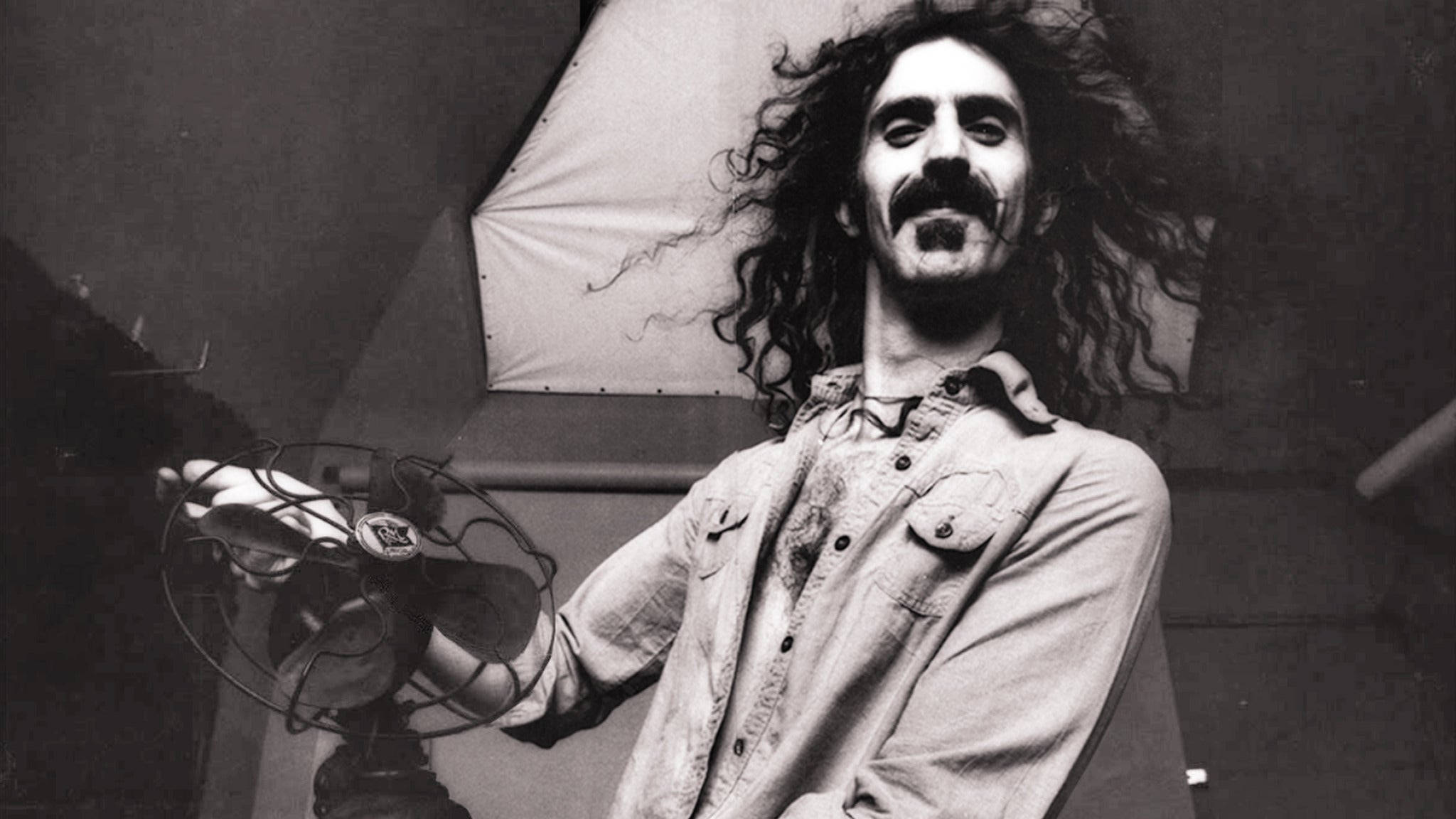 Zappa 桌布 壁紙 — 一個黑白肖像，一個擁有狂野捲髮和鬍子的男人在工作室環境中拿著復古扇子。
