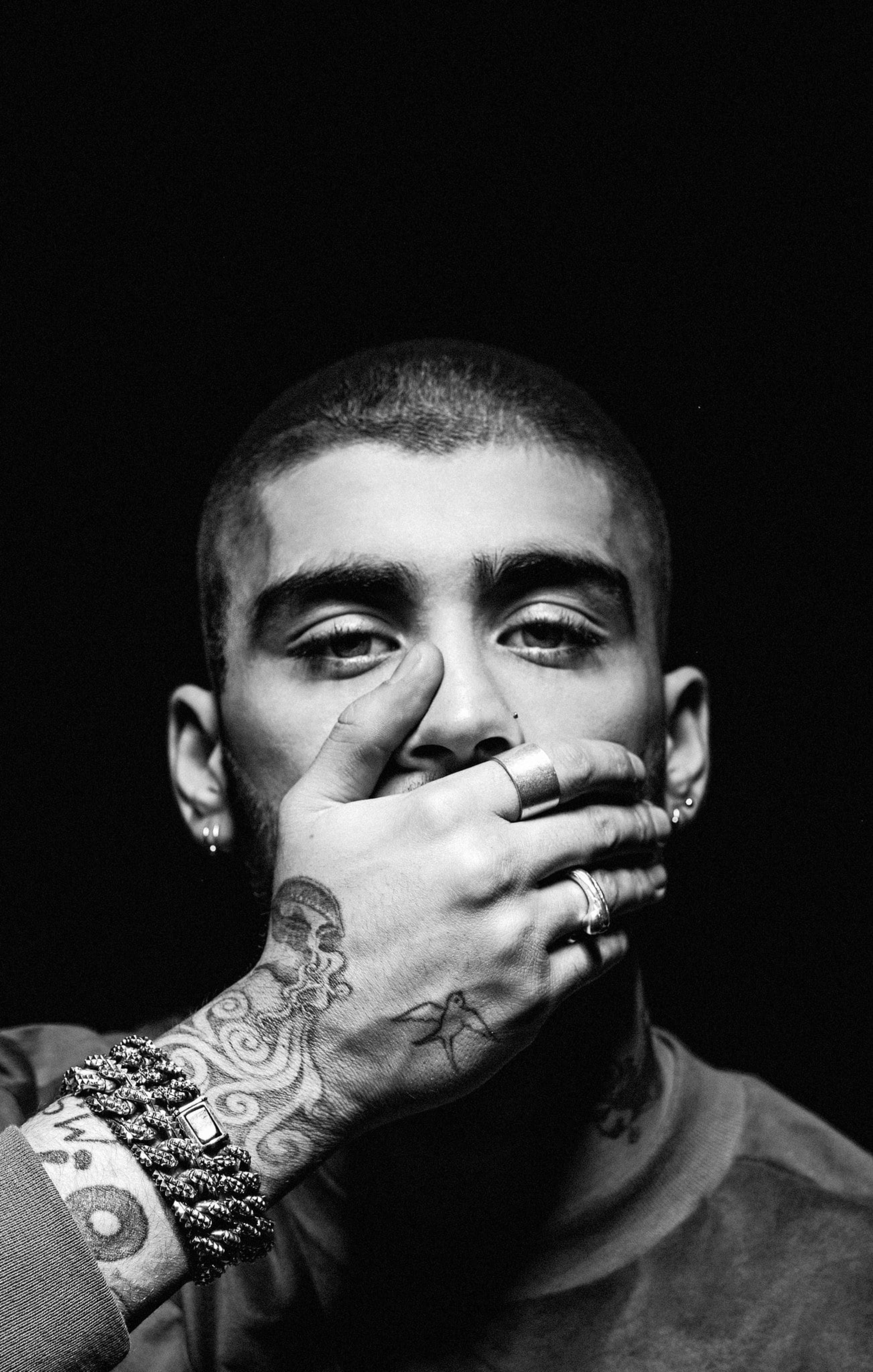 zayn 桌布 壁紙 — 一個黑白肖像，一個男人手上和手腕上有刺青，用手遮住嘴巴，背景黑暗。
