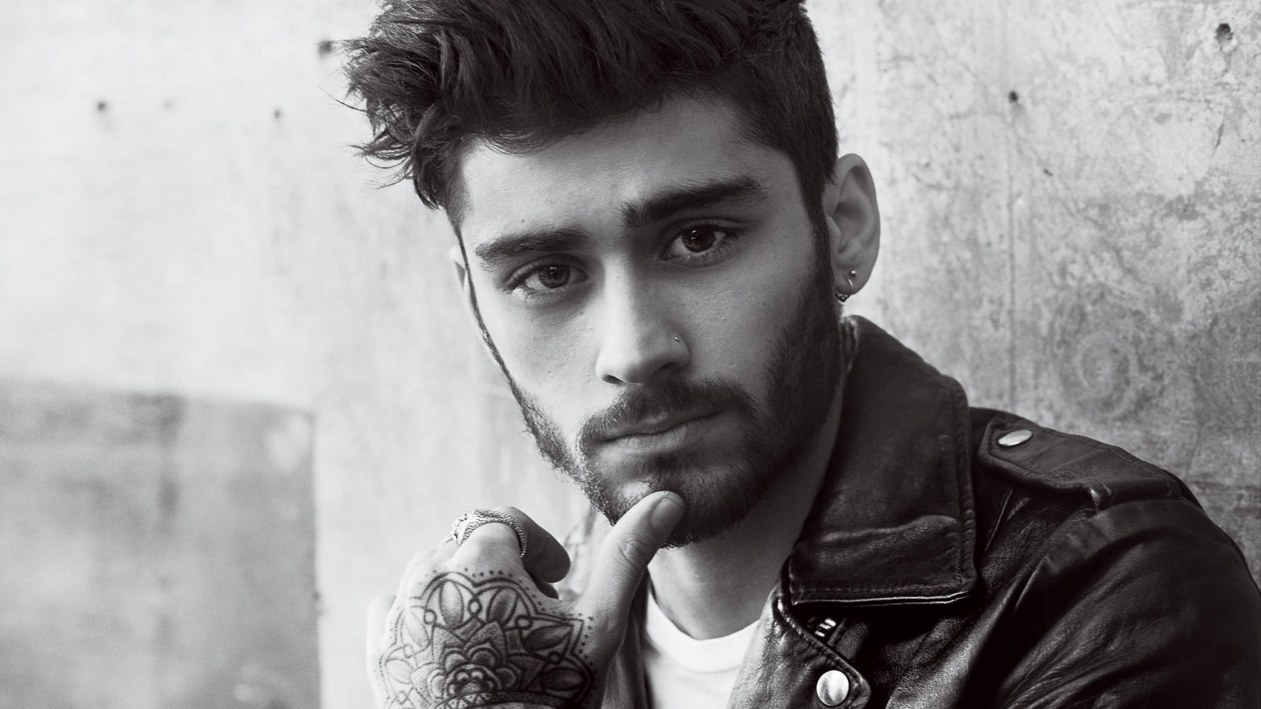 zayn 桌布 壁紙 — 一個黑白肖像，一個留鬍鬚、手上有刺青的男人，手托下巴，靠著紋理牆壁。