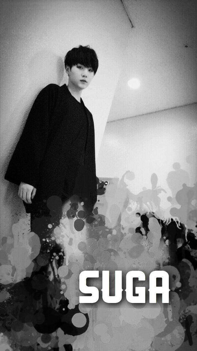 Suga Bts 桌布 壁紙 — 一個黑白肖像，一個穿著深色外套的年輕男子靠著牆，帶有抽象墨水飛濺和下方粗體文字。
