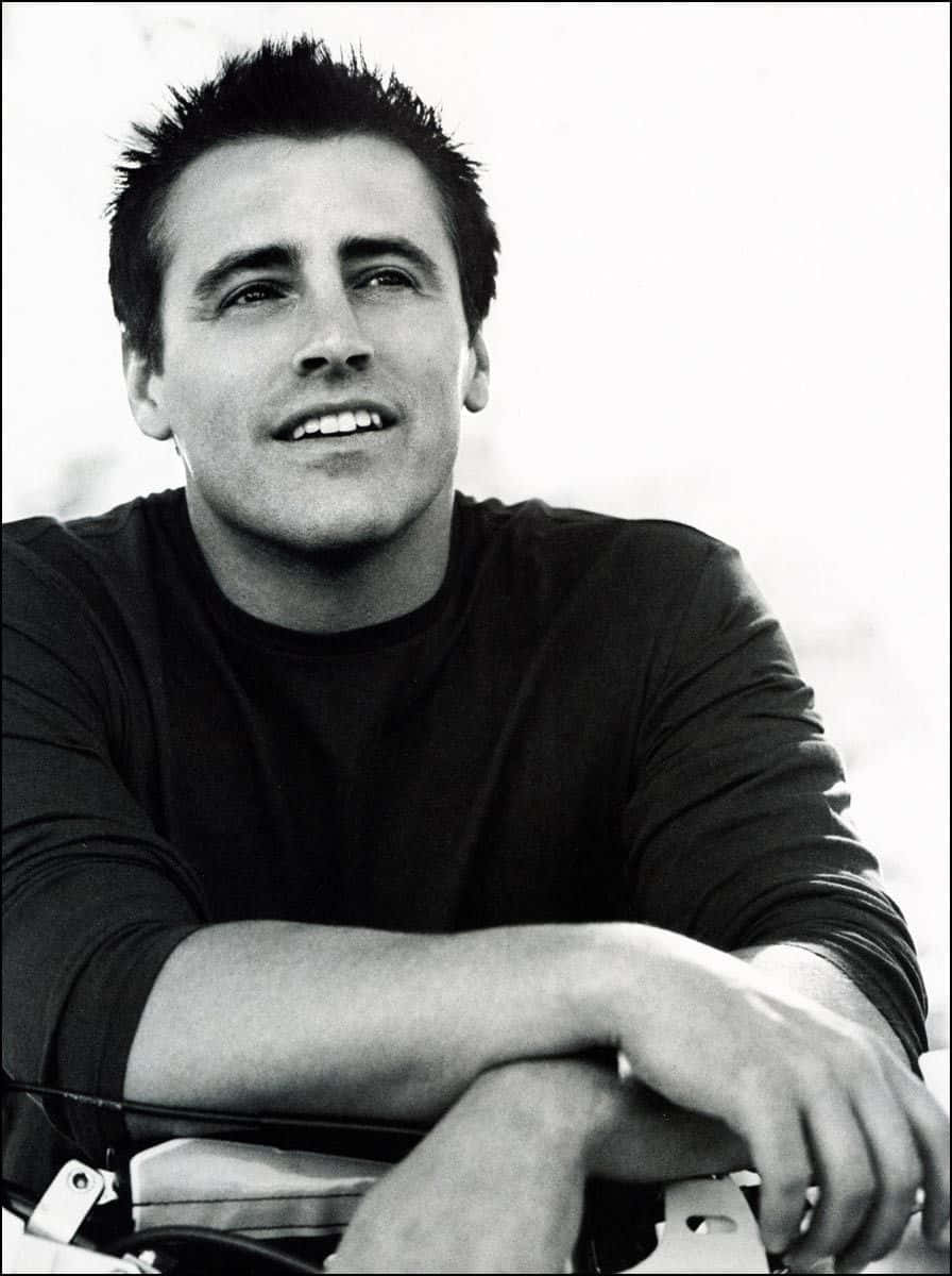 Matt Leblanc 桌布 壁紙 — 一個黑白肖像，一個笑容滿面、頭髮豎起的男人靠在汽車引擎蓋上。
