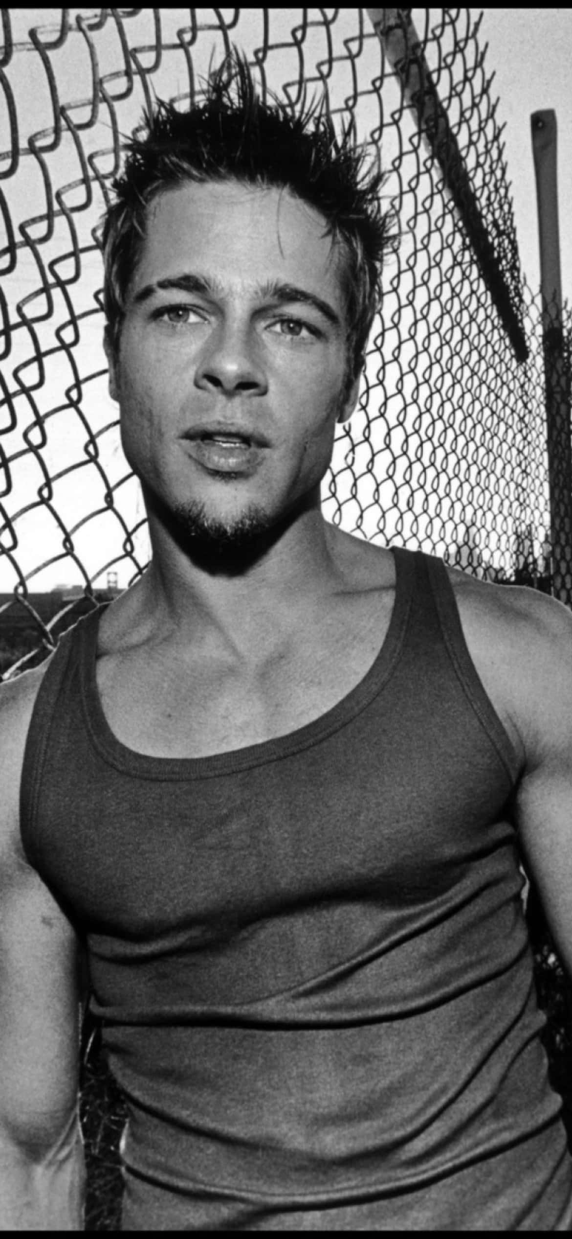 Brad Pitt 桌布 壁紙 — 一個黑白肖像，一個頭髮尖刺、鬍渣的男人穿著背心，靠在鐵絲網圍欄上。