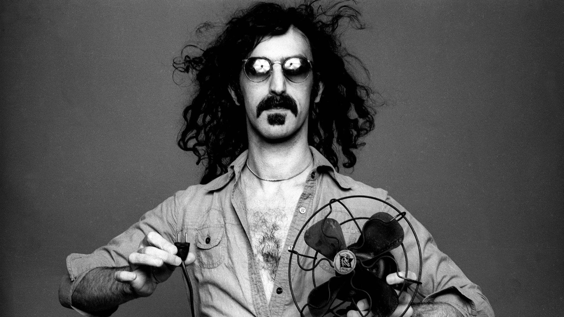 Zappa 桌布 壁紙 — 一個黑白肖像，一個頭髮狂野、戴著太陽眼鏡的男人，手持風扇和插頭。