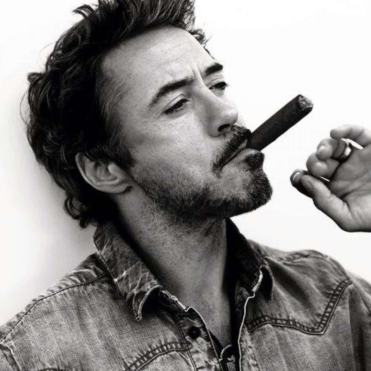 actor 桌布 壁紙 — 一個黑白肖像，一個頭髮蓬亂、留鬍子的男人，在純色背景前將雪茄放在唇邊。
