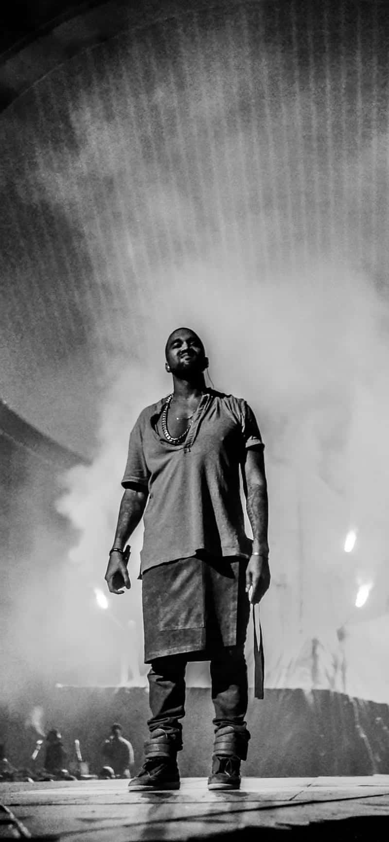 kanye iPhone 桌布 壁紙 — 一個黑白肖像，一名男子在戲劇性燈光和煙霧中自信地站在舞台上。