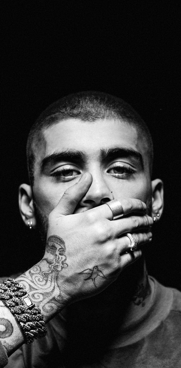 One Direction 桌布 壁紙 — 一個黑白肖像，一名男子手上和手腕佈滿刺青，在深色背景下用手指摀住嘴巴。