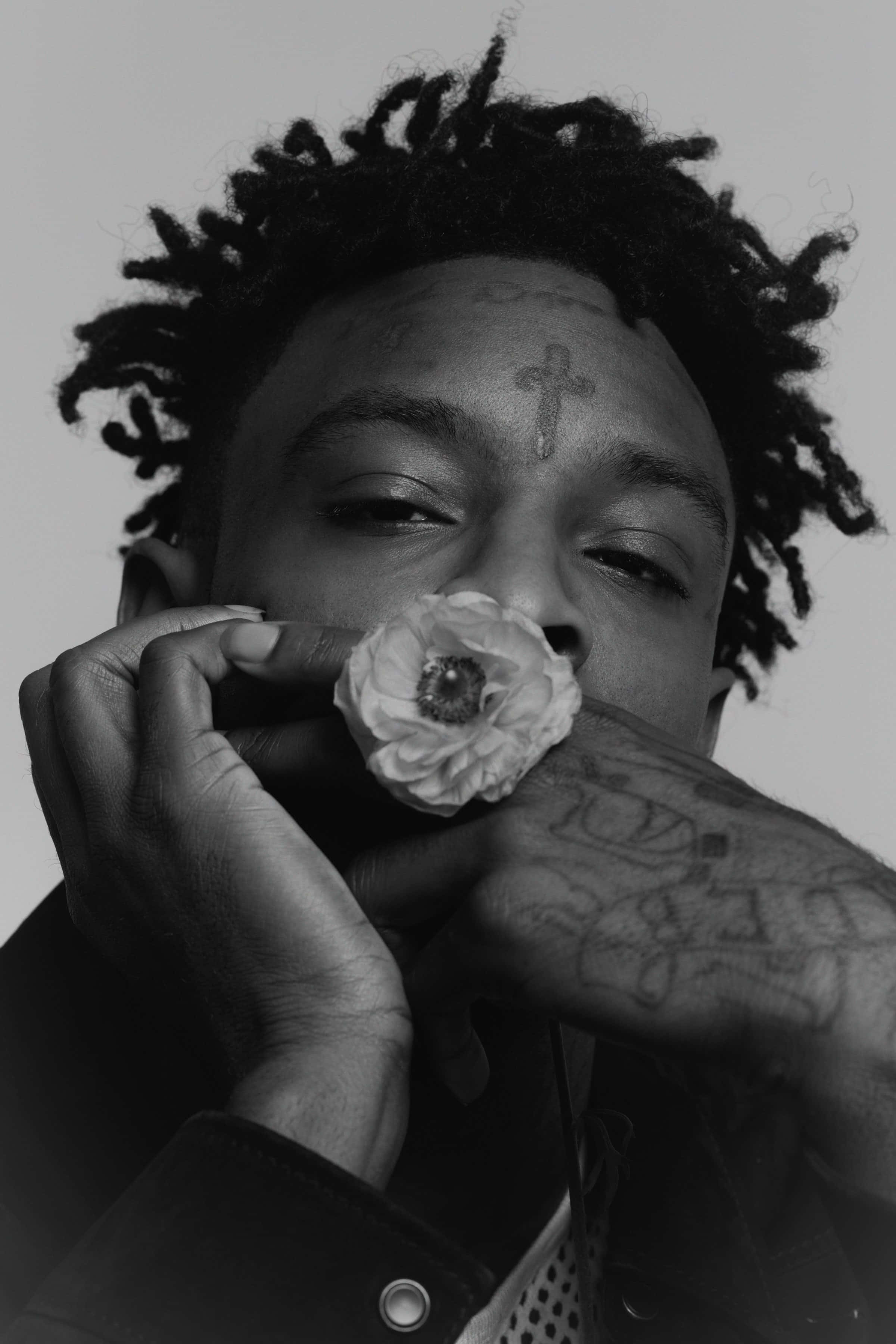 21 Savage 桌布 壁紙 — 一個黑白肖像，一名留著辮子頭的男人手持花朵靠近臉部，手臂和額頭上的刺青清晰可見。