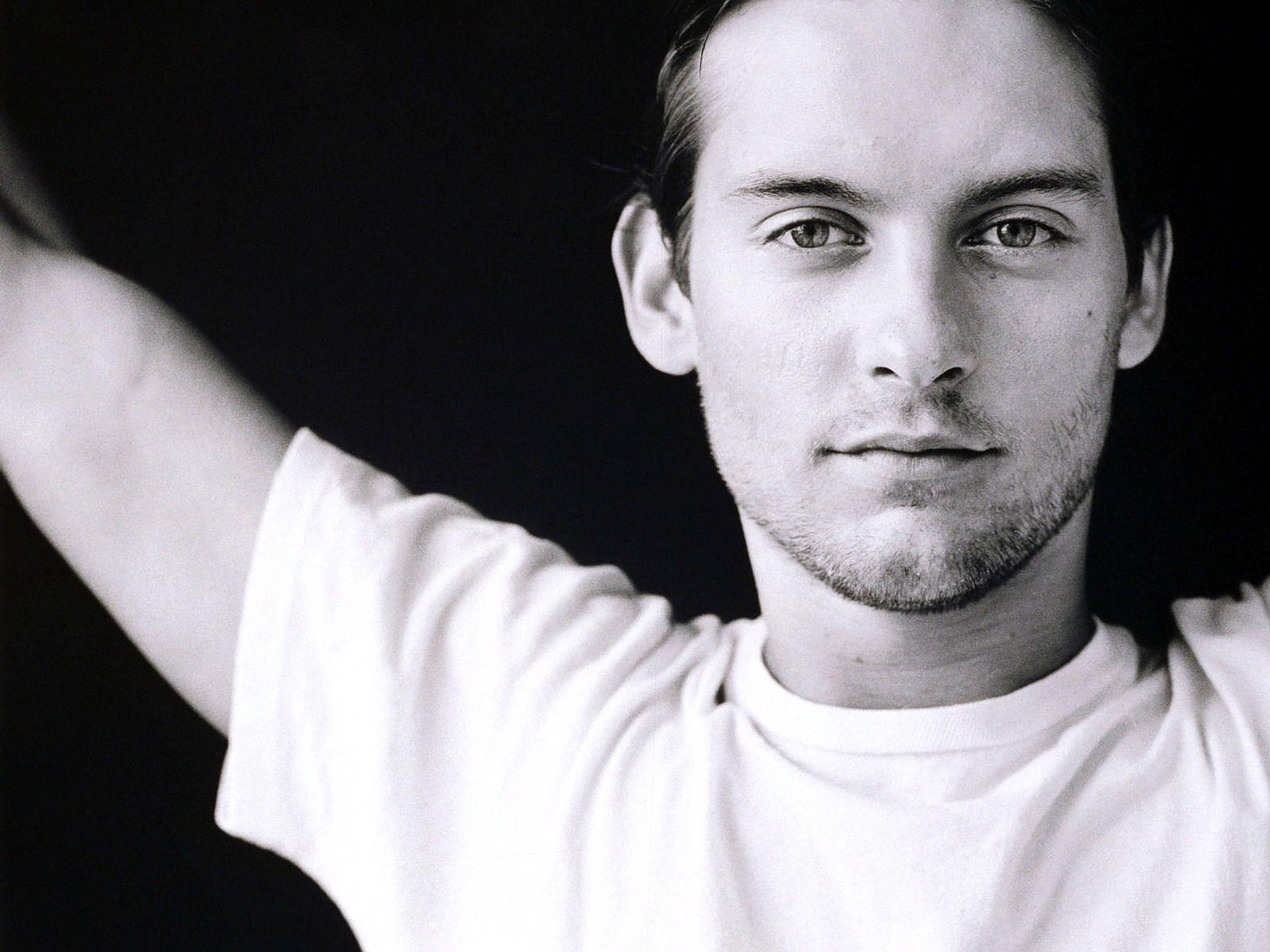 Tobey Maguire 桌布 壁紙 — 一個黑白肖像，一名身穿白色T恤的男子在深色背景前舉起一隻手臂。