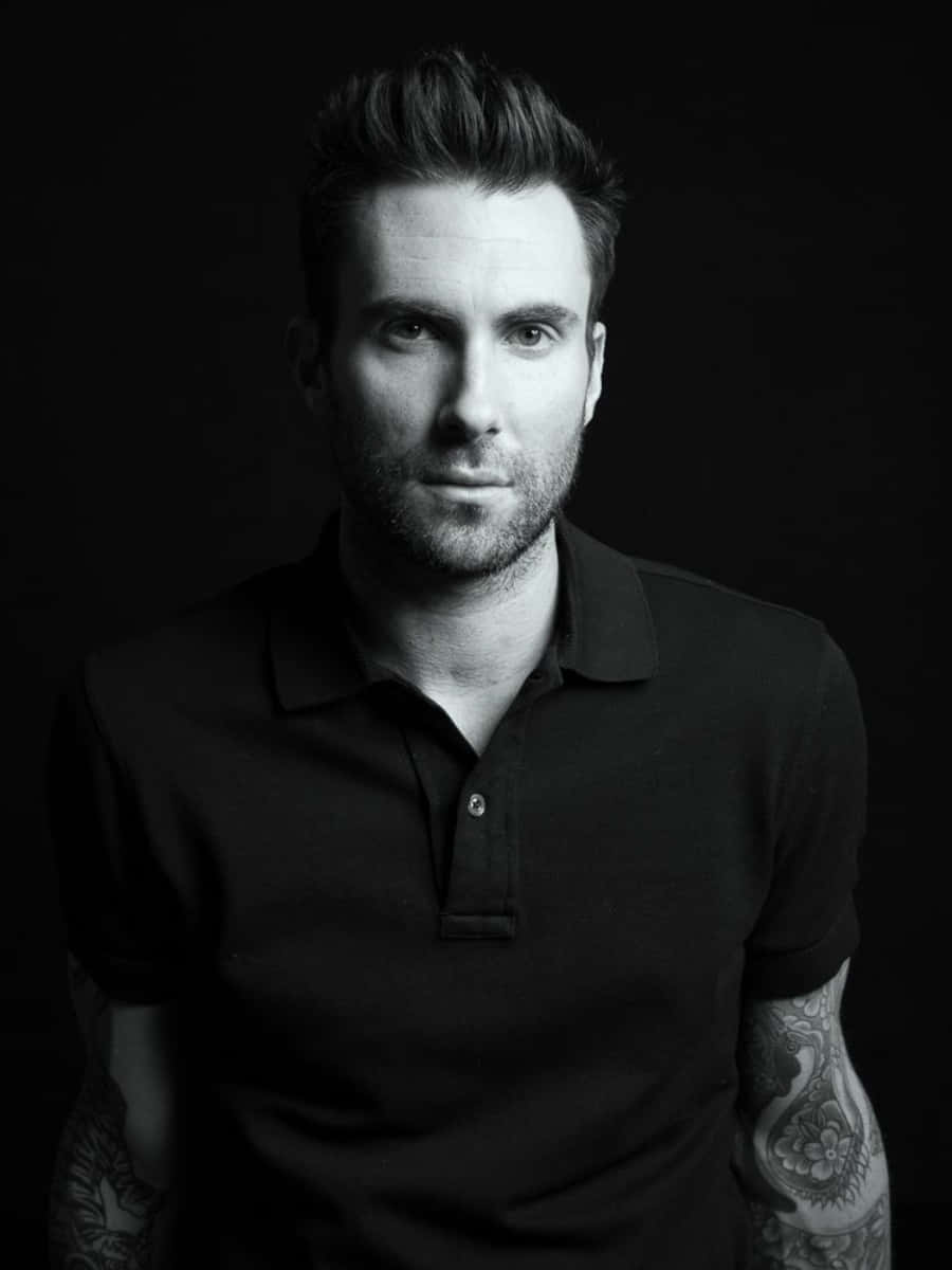 Adam Levine 桌布 壁紙 — 一個黑白肖像，展示一位手臂上有刺青的男士，穿著深色Polo衫，背景為黑色。