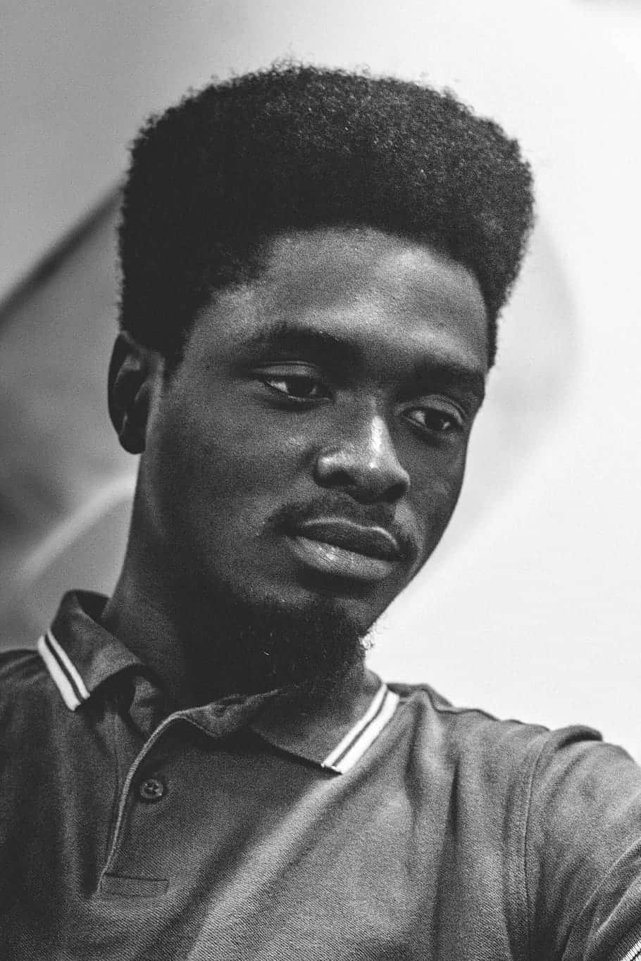 Nigeria 桌布 壁紙 — 一個黑白肖像，年輕男子帶有紋理的爆炸頭和襯衫，若有所思地望向鏡頭外。