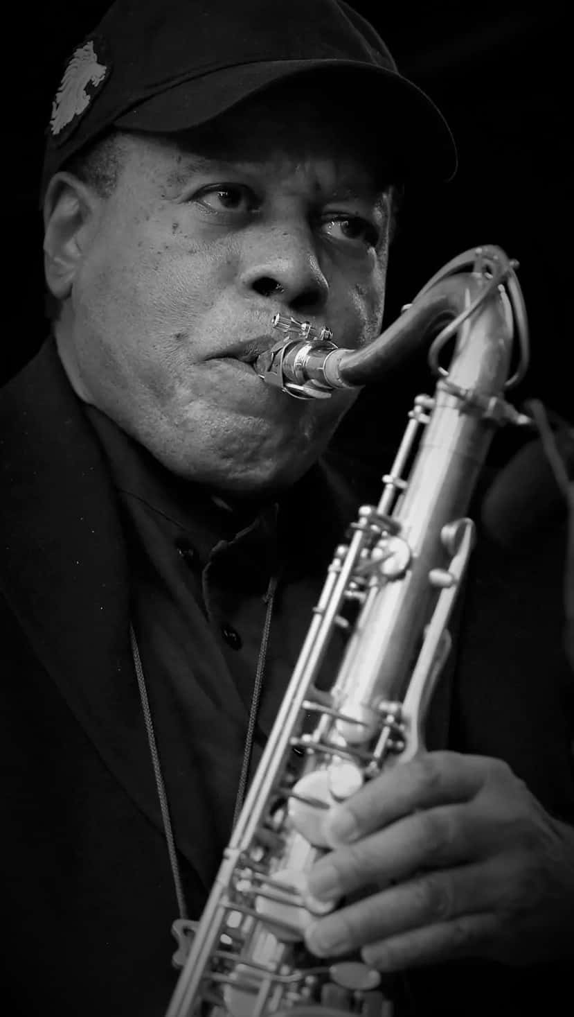 Wayne Shorter 桌布 壁紙 — 一個黑白肖像，捕捉一名男子專注地吹奏薩克斯風的強烈神情。