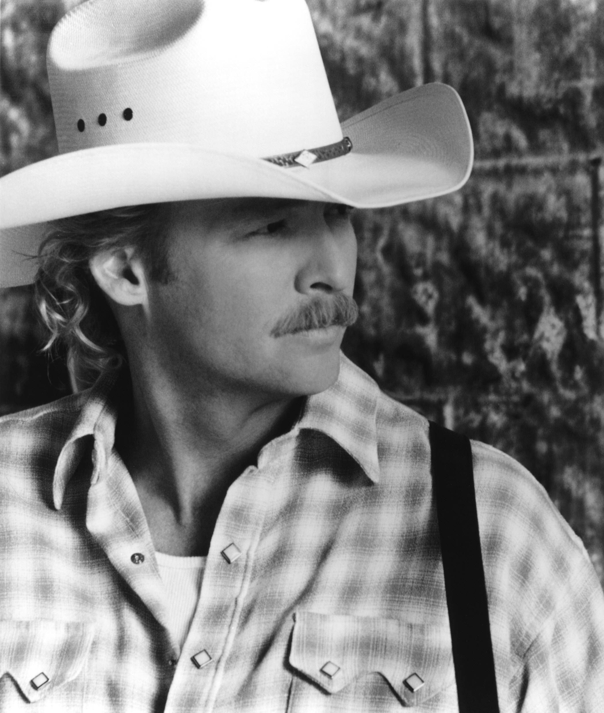 Alan Jackson 桌布 壁紙 — 一個黑白肖像，描繪一位留鬍子的牛仔，戴著白色帽子，穿著格紋襯衫，背景是質感石牆。