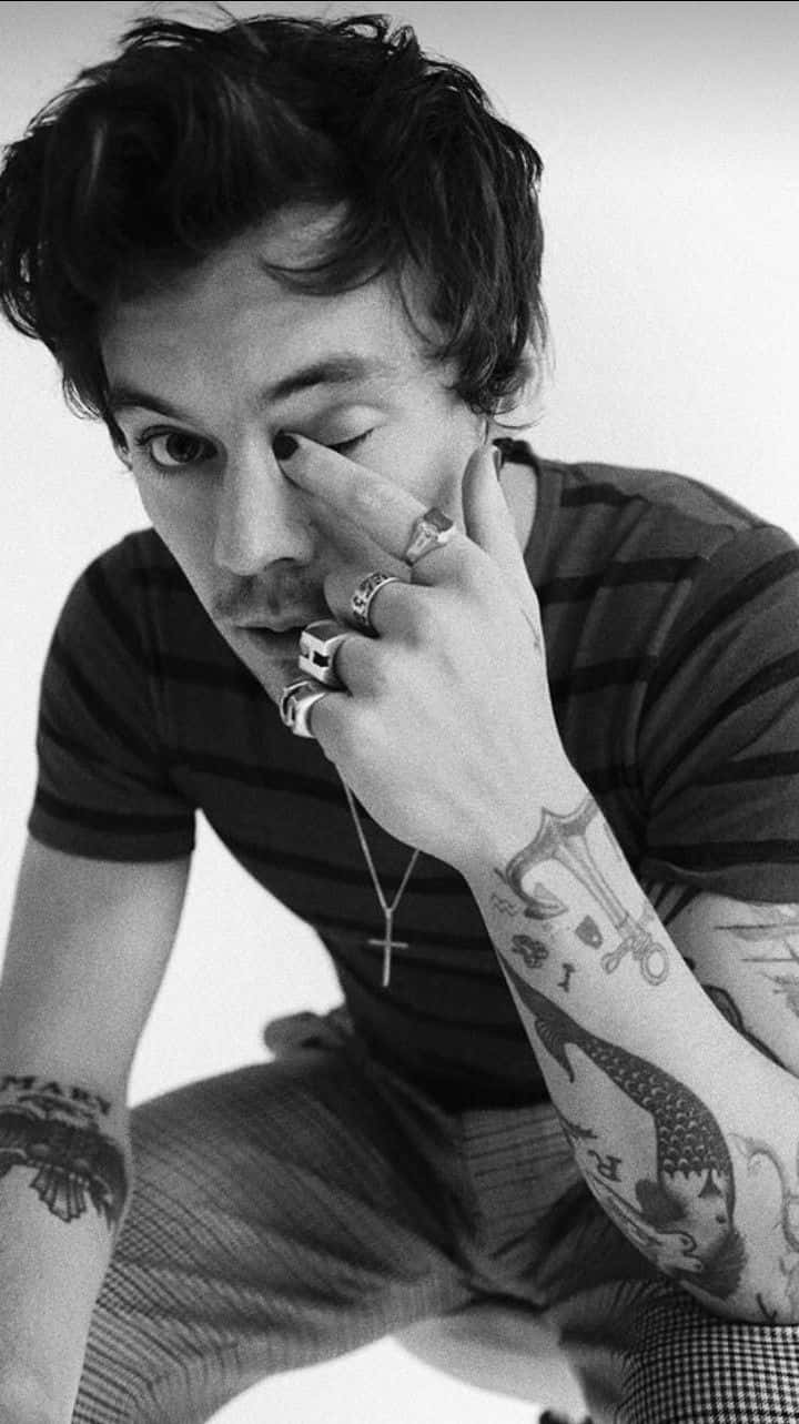Harry Styles Black And White 桌布 壁紙 — 一個黑白肖像，描繪一位紋身男子，深色頭髮，用戴著戒指的手觸碰眼睛。