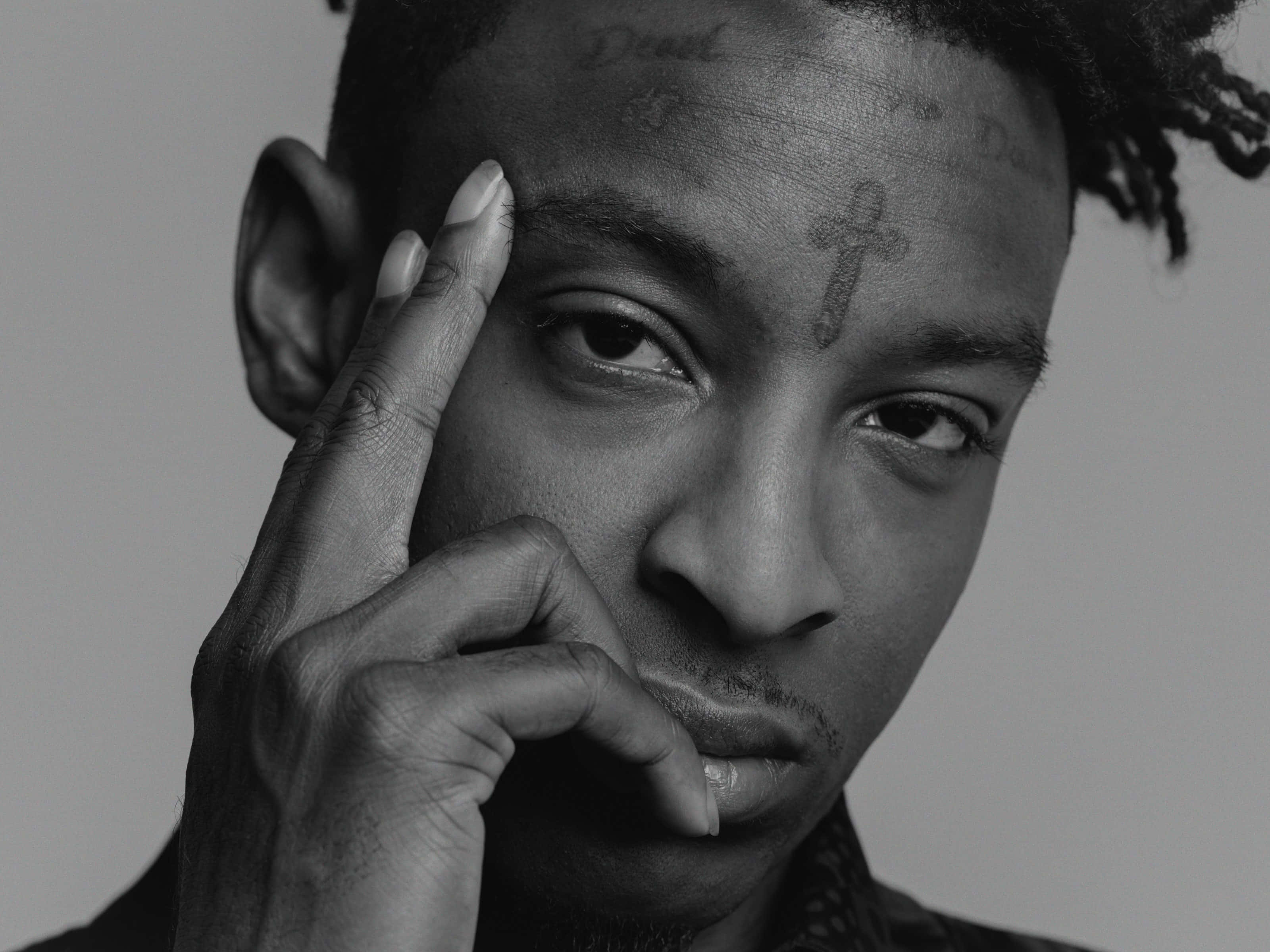 21 Savage 桌布 壁紙 — 一個黑白肖像，男人額頭上有刺青，手放在臉附近。