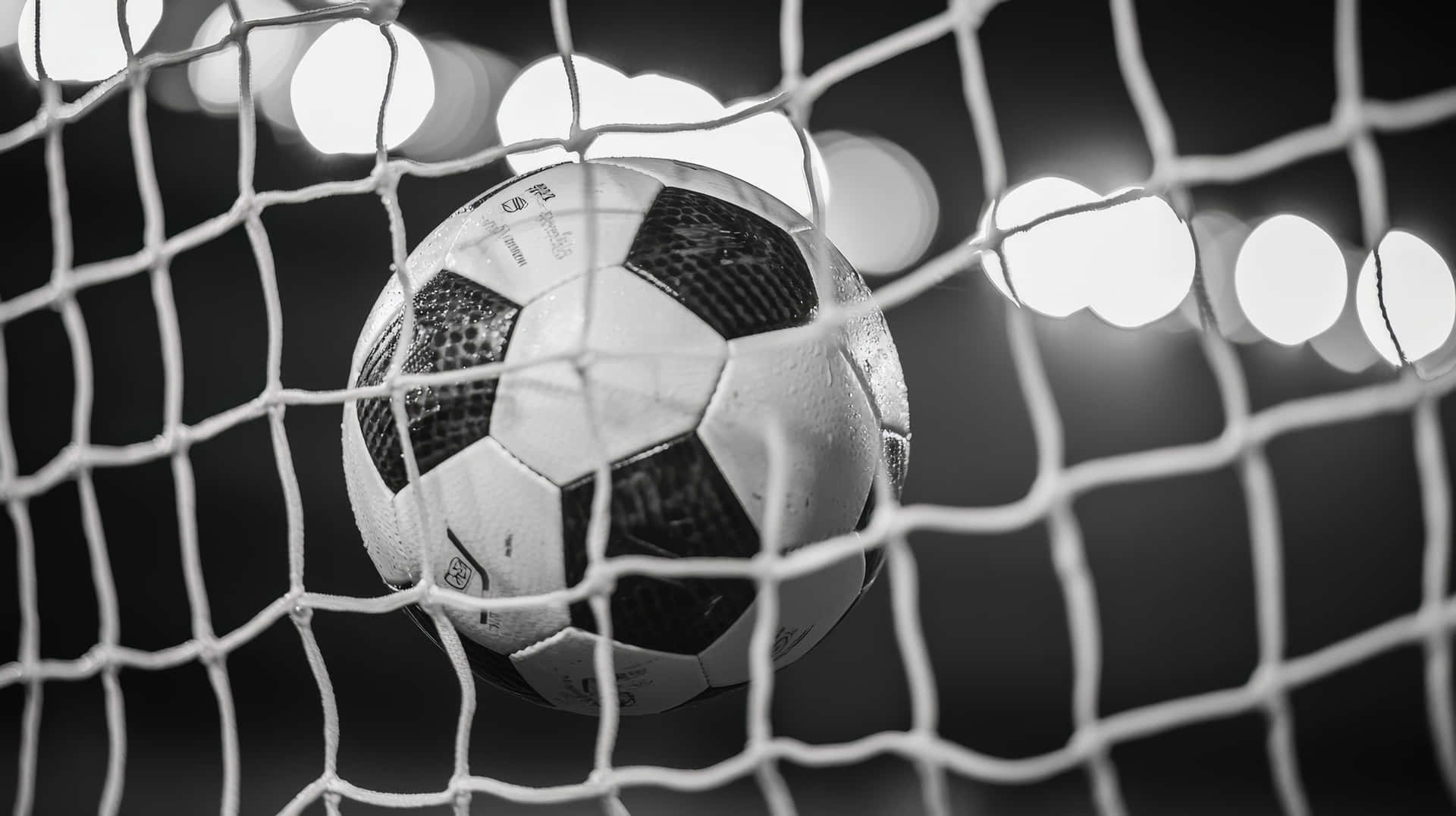 Black and White Soccer Ball Scoring a Goal in Net Under Stadium Lights 壁紙 — 一個黑白足球放在網中，背景有模糊的球場燈光。