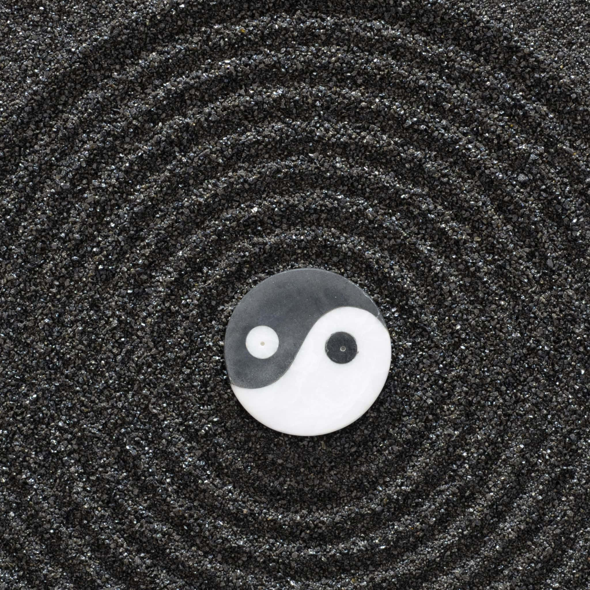 Ying Yang 桌布 壁紙 — 一個黑白陰陽符號放置在耙成同心圓的深色沙子上。
