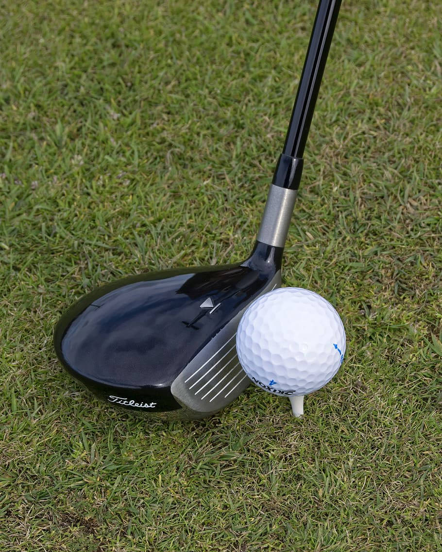 高爾夫 桌布 壁紙 — 一個黑色 Titleist 高爾夫球桿頭放在綠色草地上，旁邊有一個白色高爾夫球在 tee 上。