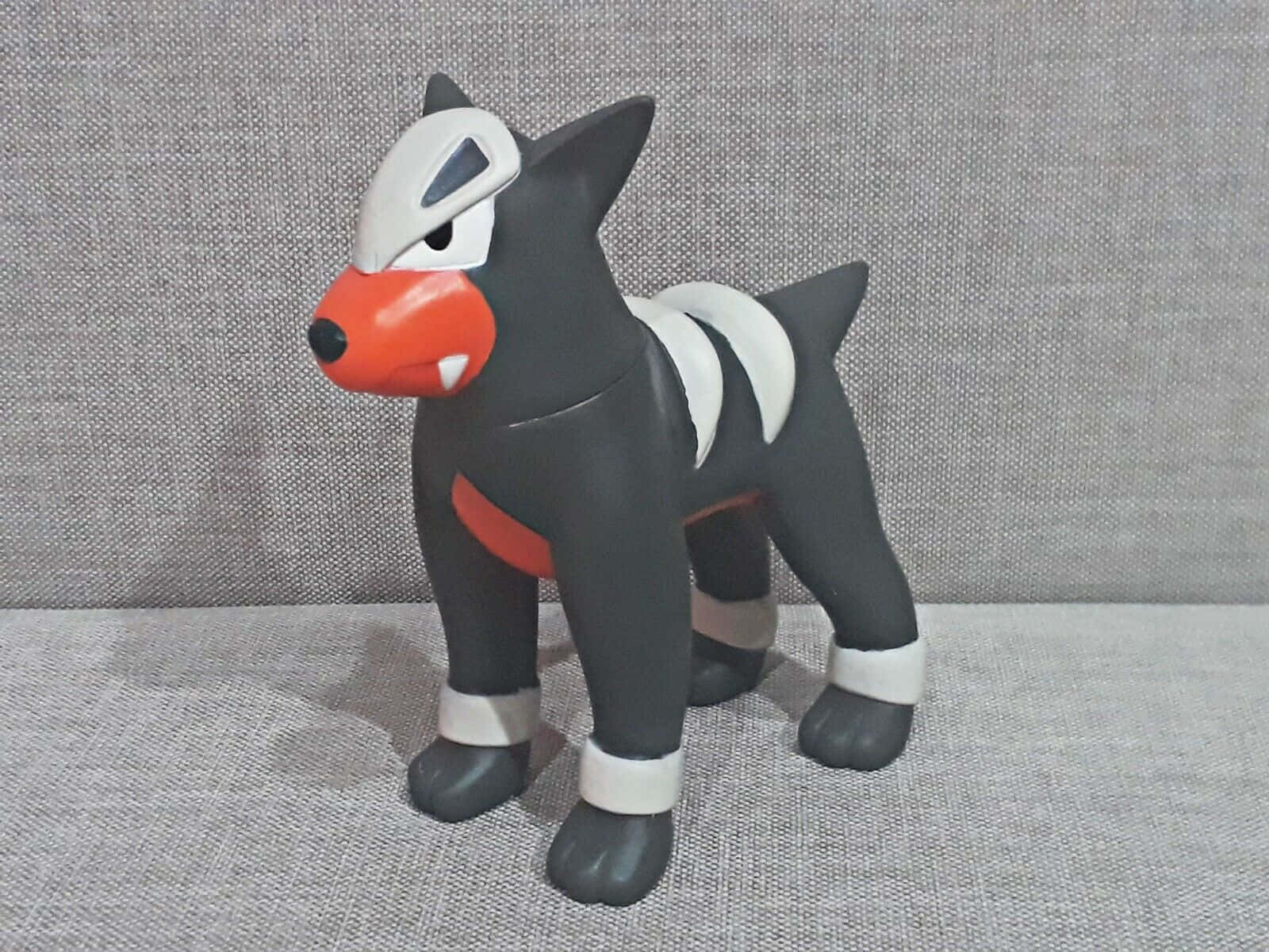 狗 桌布 壁紙 — 一個黑色、白色和橙色的 Houndour 寶可夢公仔警覺地站在灰色紋理表面上。