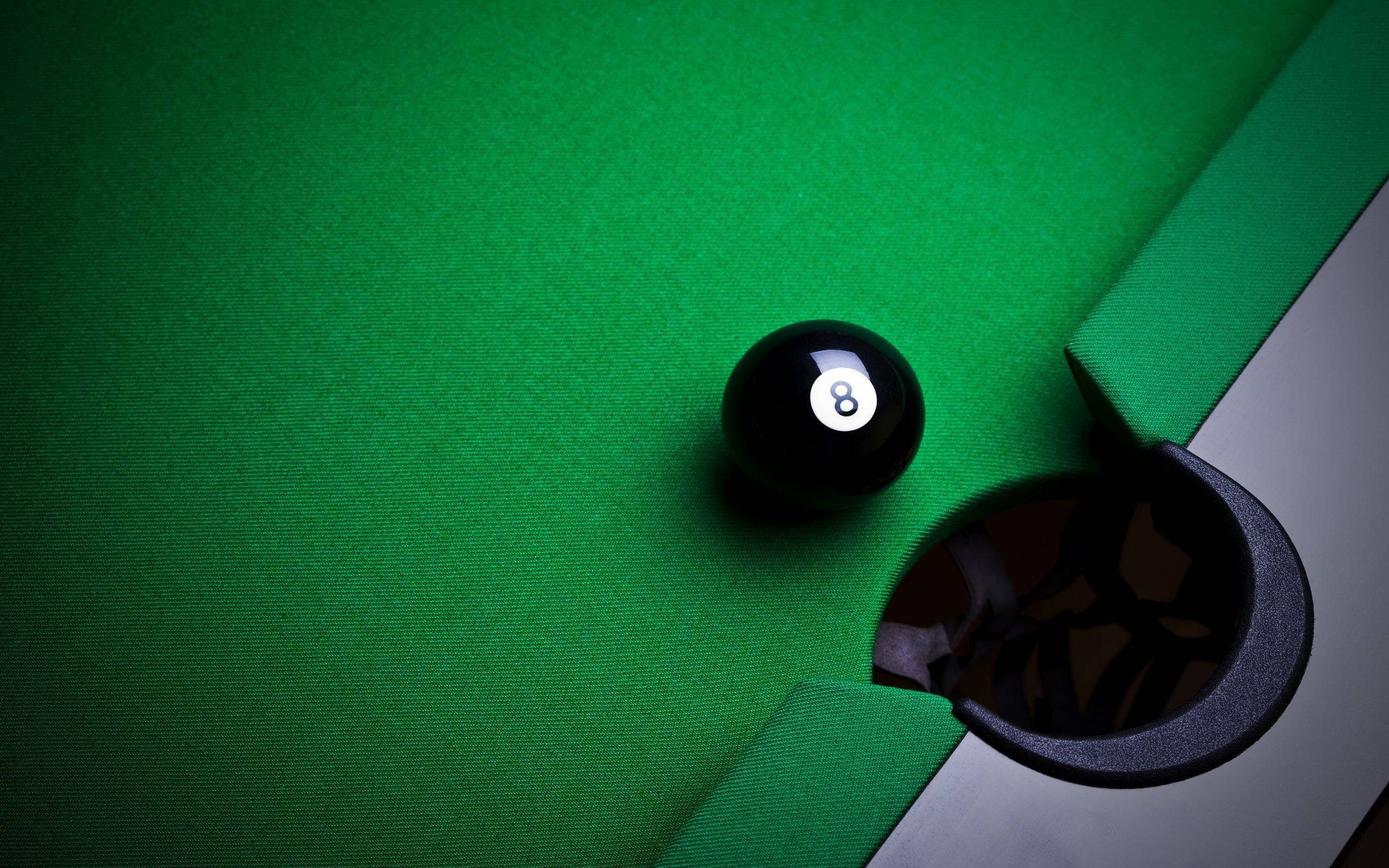 Snooker 桌布 壁紙 — 一個黑色8號球放在一張充滿活力的綠色撞球桌上，靠近球袋，燈光效果戲劇化。