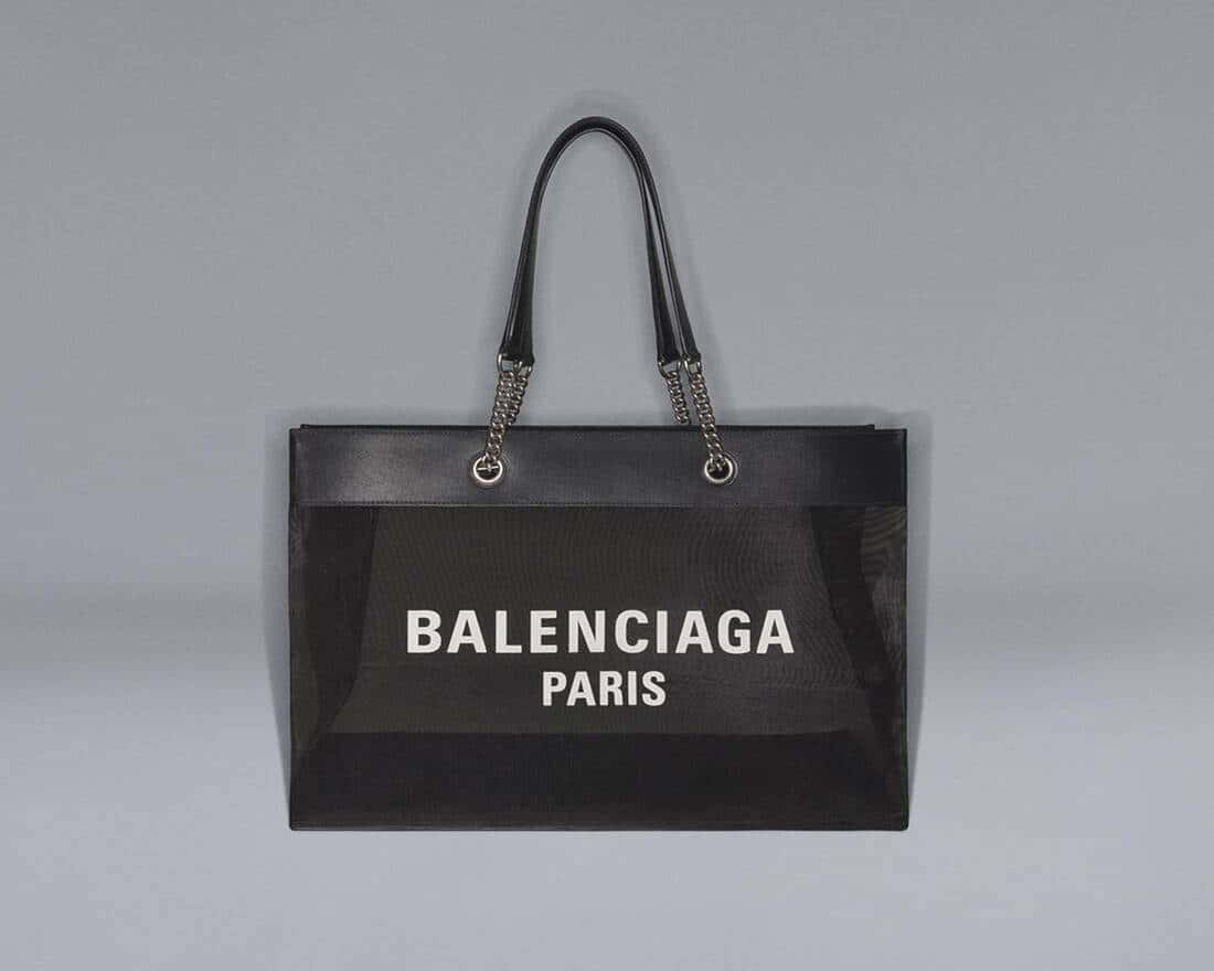 巴黎世家 桌布 壁紙 — 一個黑色Balenciaga Paris手提袋，正面網眼設計，鏈條手柄，掛在純灰色背景上。