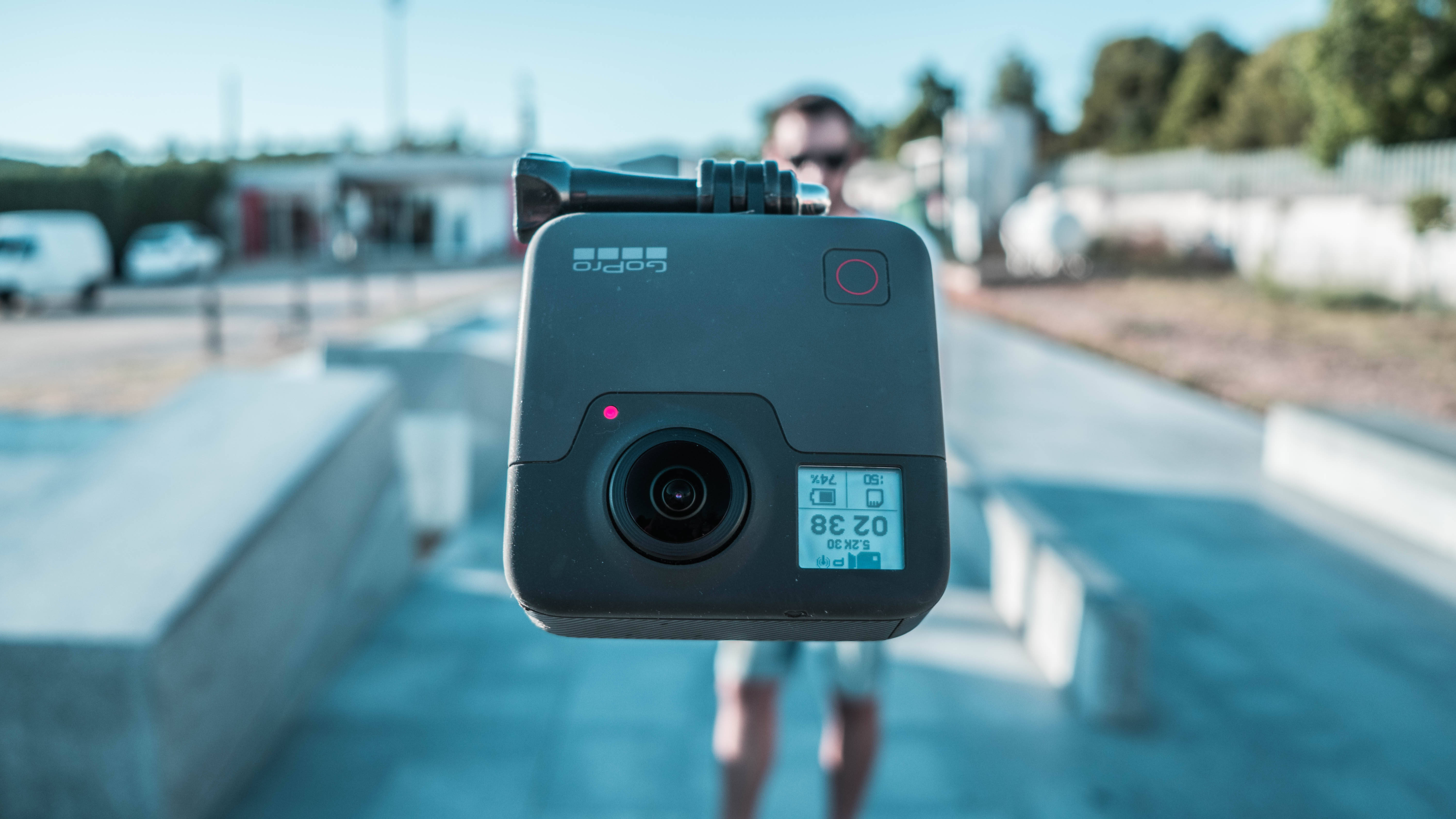 Webcam 桌布 壁紙 — 一個黑色GoPro相機的特寫，背景中有一個人模糊不清，在陽光明媚的日子裡。
