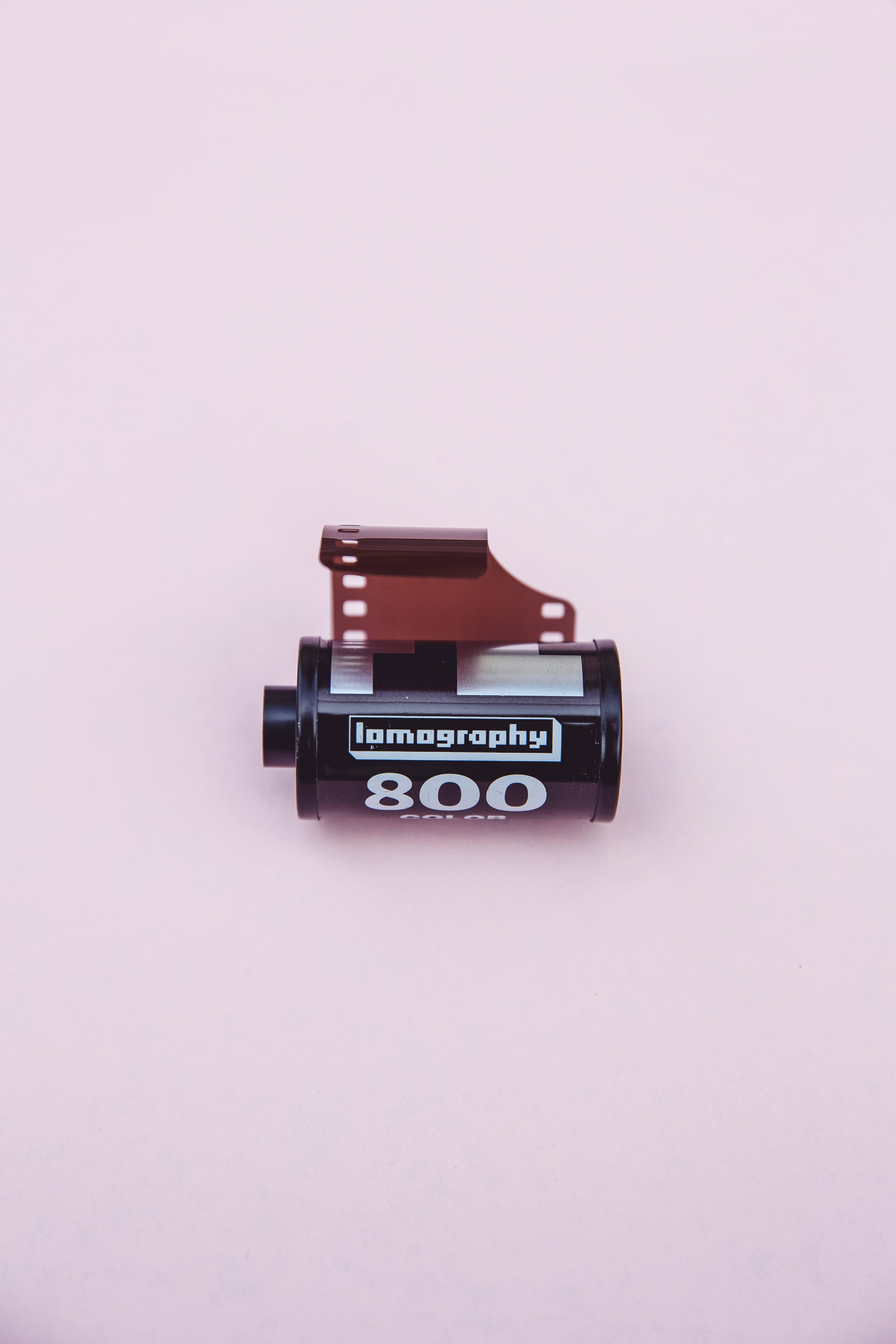 電影 桌布 壁紙 — 一個黑色Lomography 800底片罐連同已曝光的底片條放在柔和的粉紅色背景上。