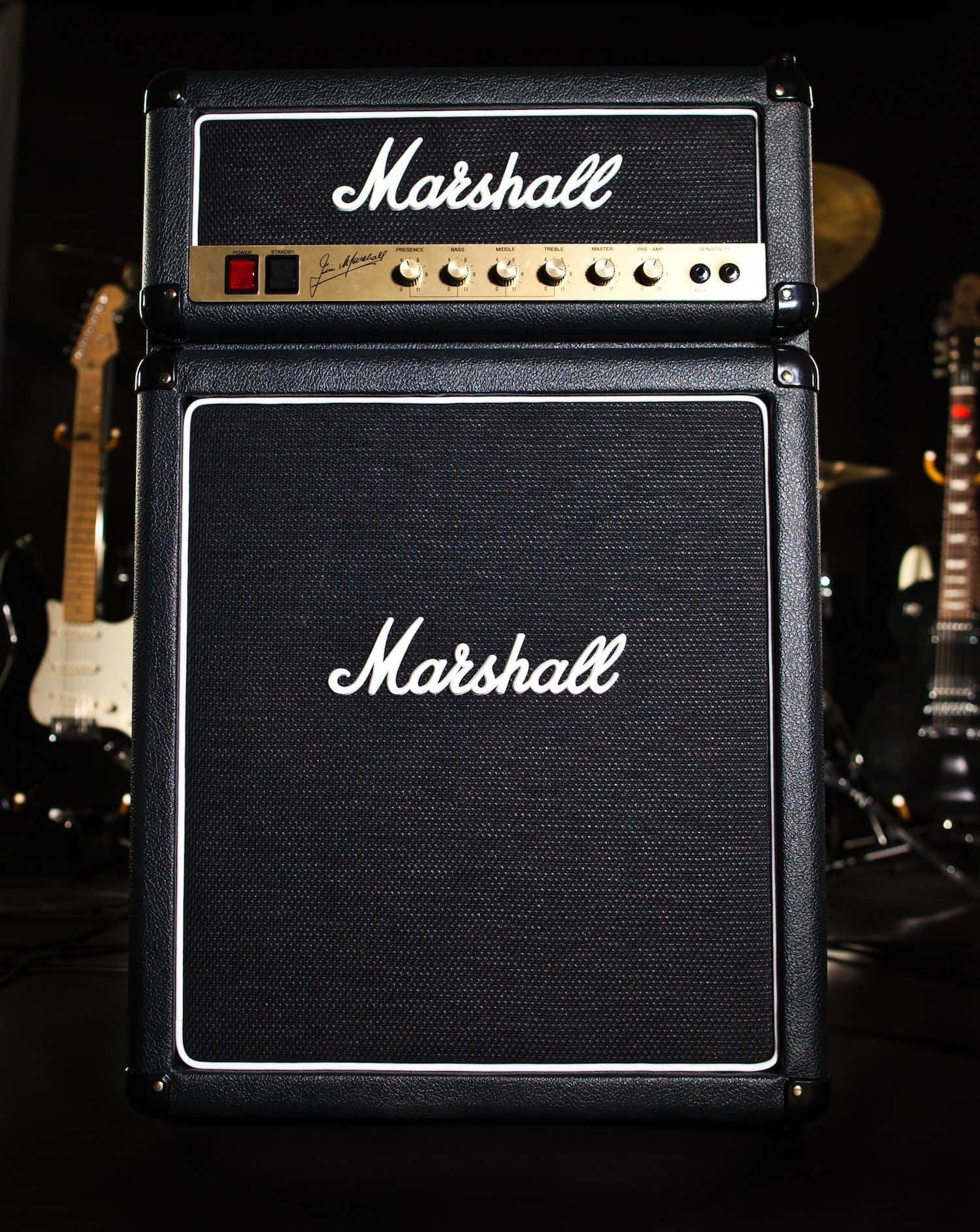 Guitar Amp 桌布 壁紙 — 一個黑色Marshall吉他擴音器，帶有白色標誌和金色旋鈕，站在舞台中央，在昏暗燈光下被電吉他包圍。