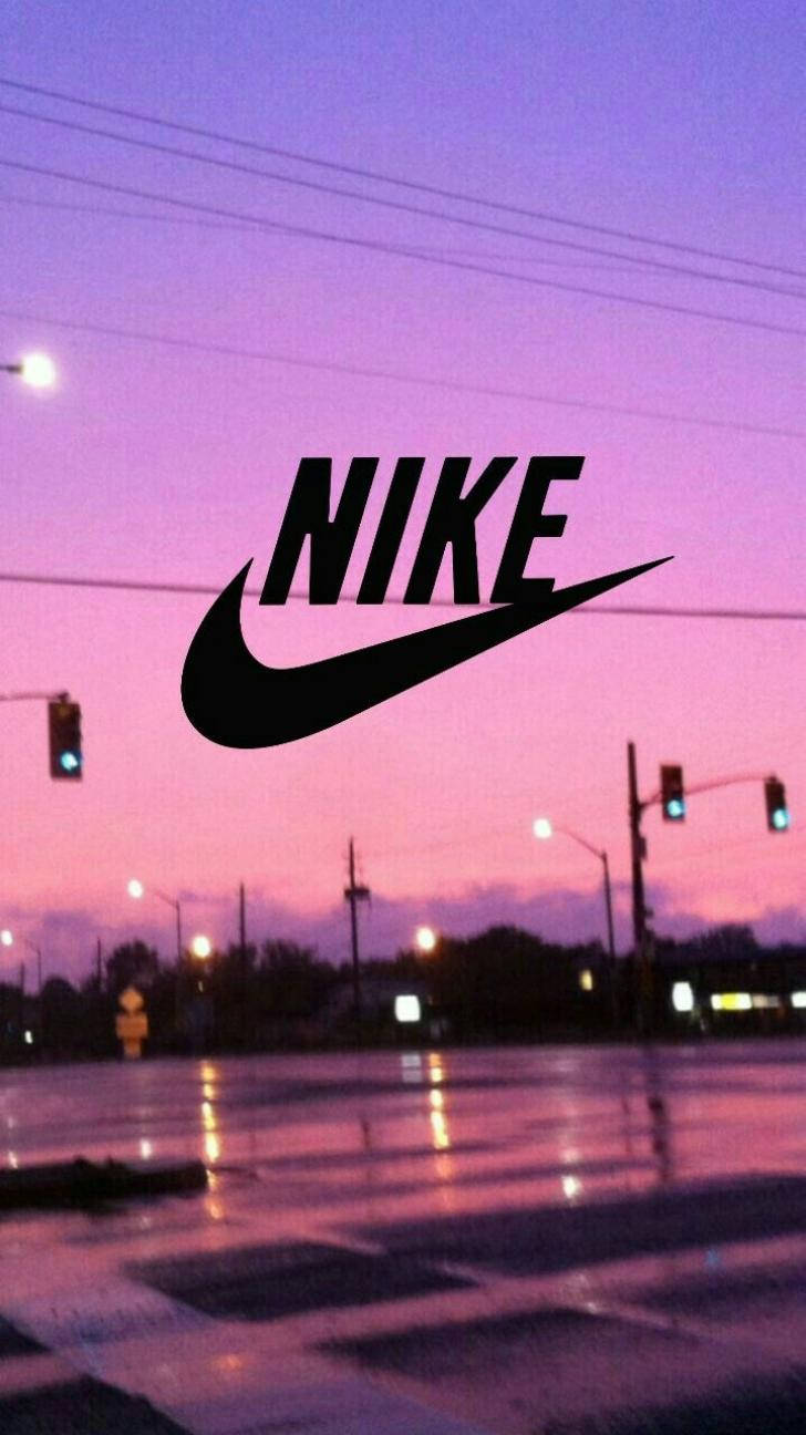Swoosh 桌布 壁紙 — 一個黑色Nike標誌漂浮在潮濕的城市街道上，黃昏時分，天空呈現粉紫色，交通燈閃爍發光。