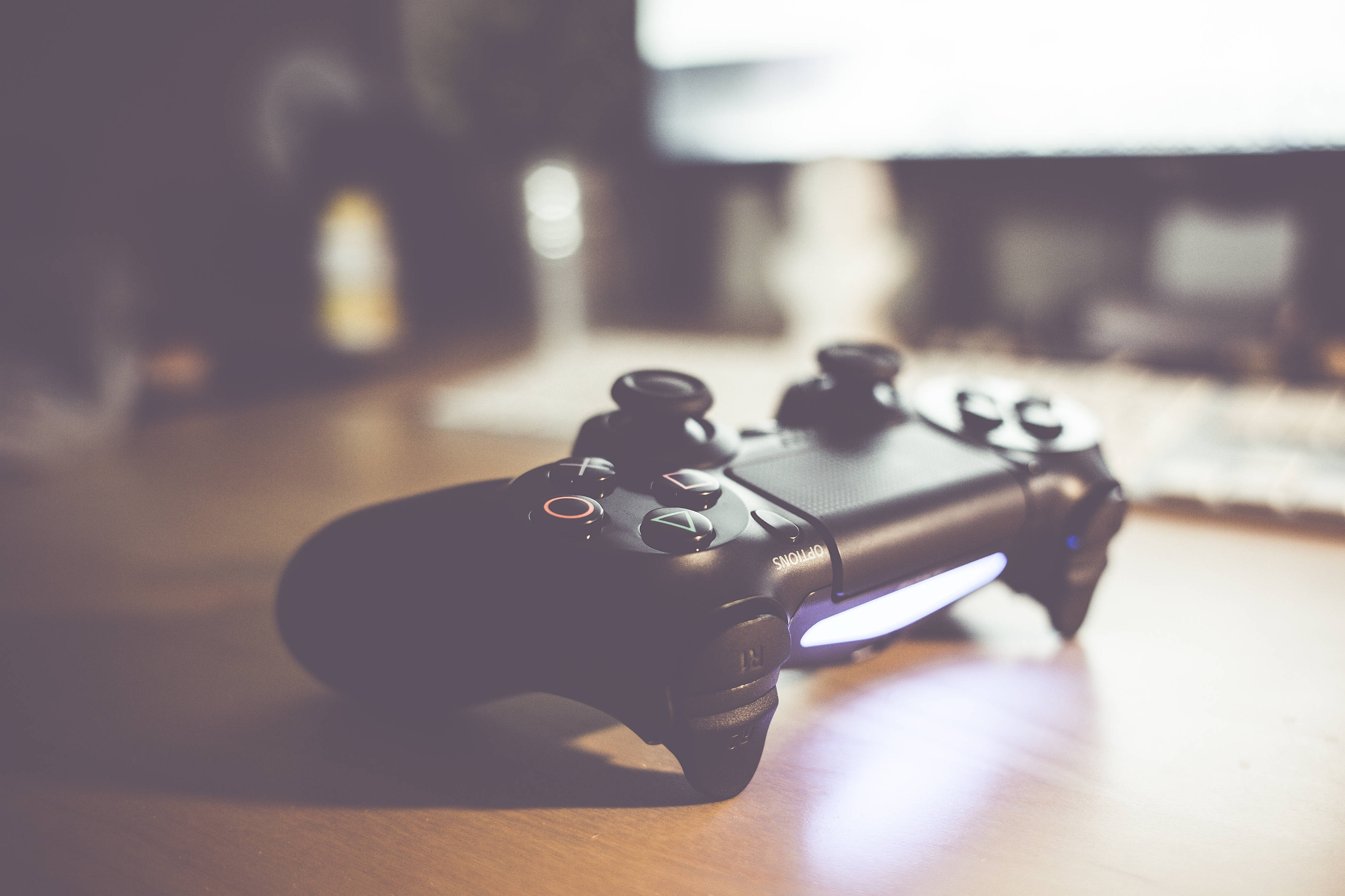 Banner 桌布 壁紙 — 一個黑色PlayStation手把放在木質表面上，帶有柔和溫暖的燈光和模糊的背景。