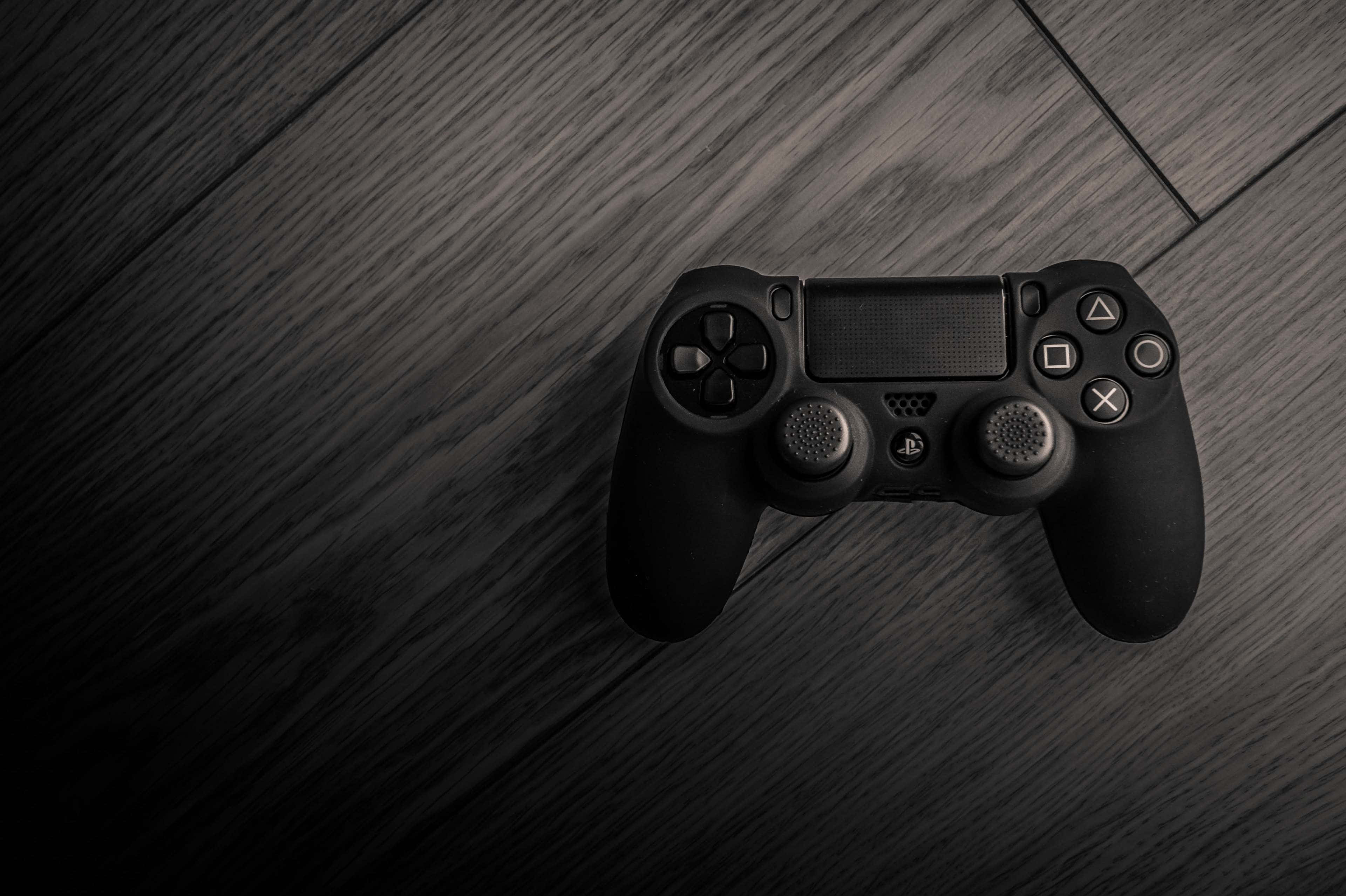 桌布 壁紙 — 一個黑色PlayStation手把放在深色木質表面上，帶有戲劇性的低調燈光。