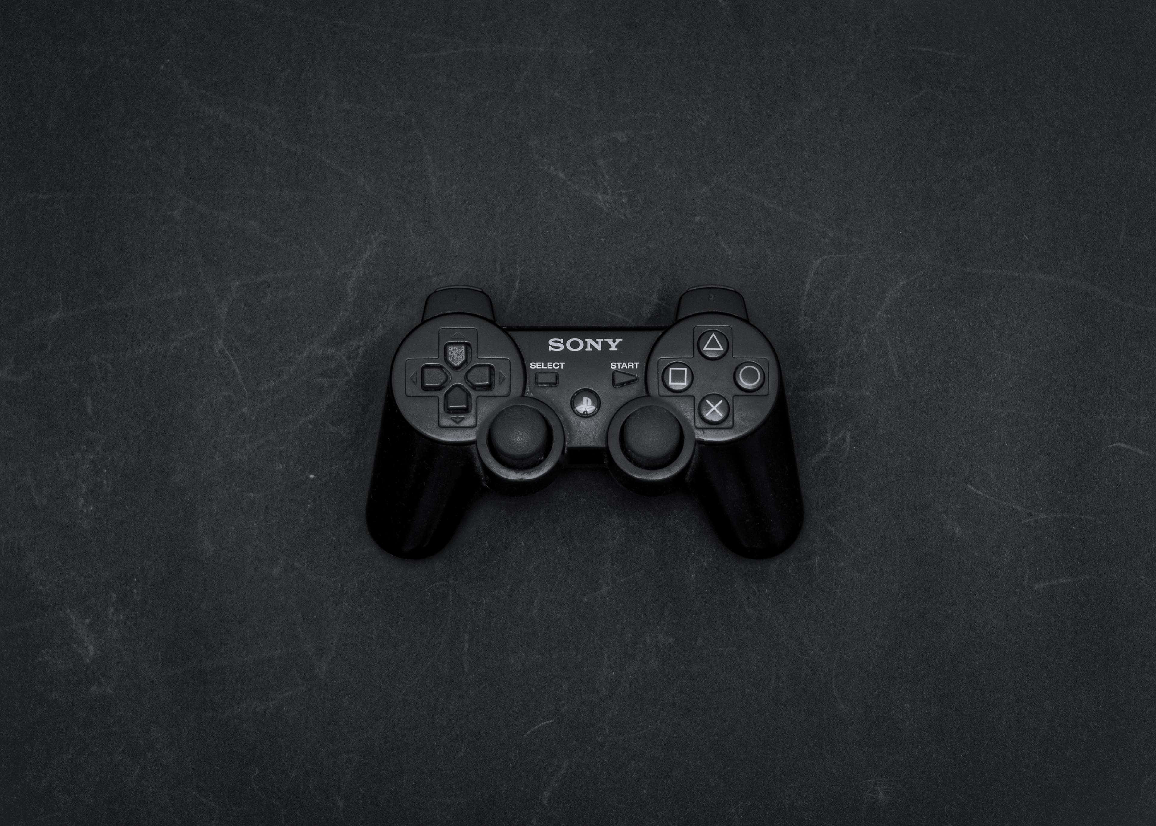 桌布 壁紙 — 一個黑色Sony PlayStation 3手把在柔和燈光下居中放在有刮痕的深灰色表面上。