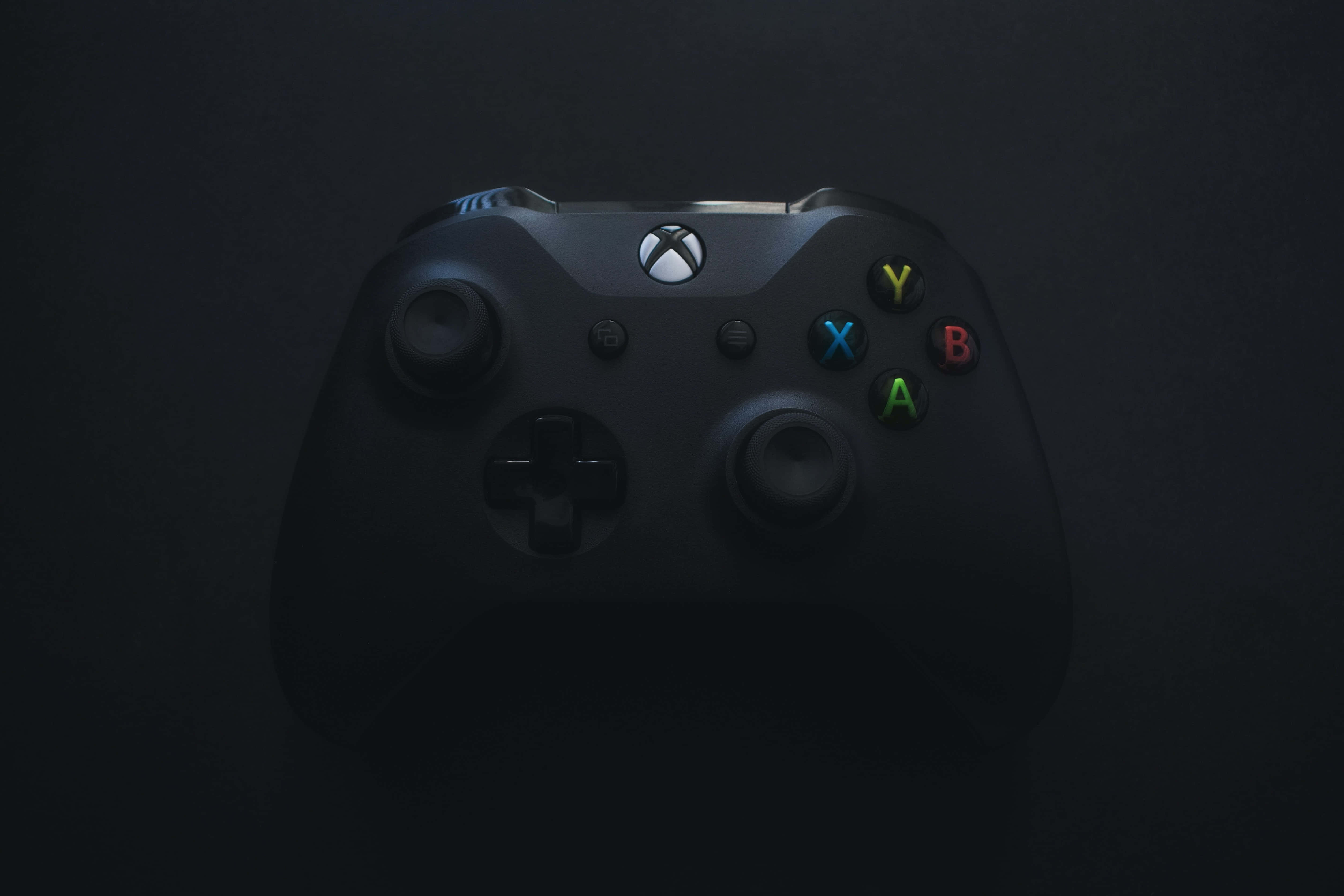 玩家 桌布 壁紙 — 一個黑色Xbox手把在深色背景上微微發光，彩色按鈕被照亮。
