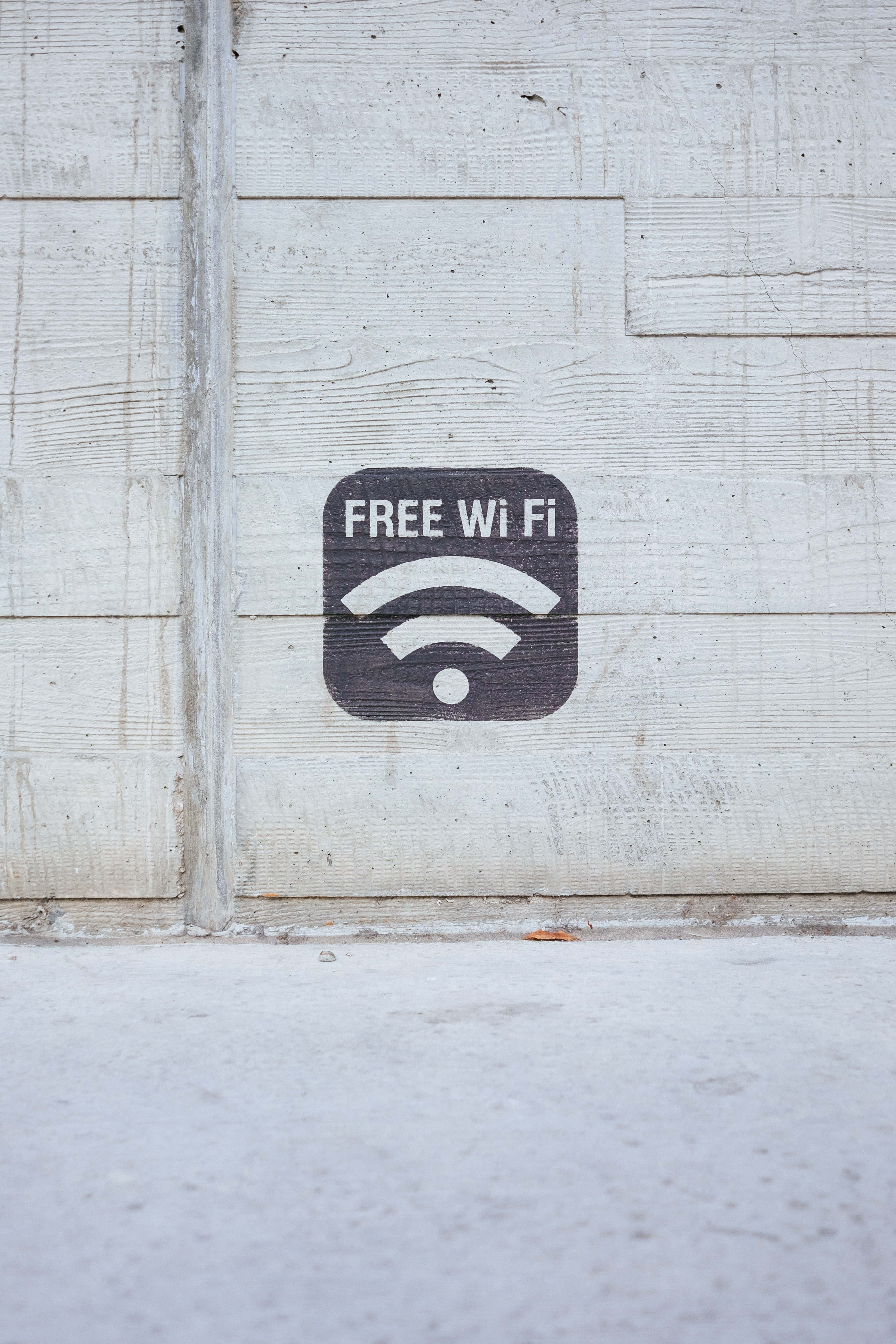 wifi 桌布 壁紙 — 一個黑色免費Wi-Fi標誌，上面有白色文字和符號，繪在經風化的白色木牆上。