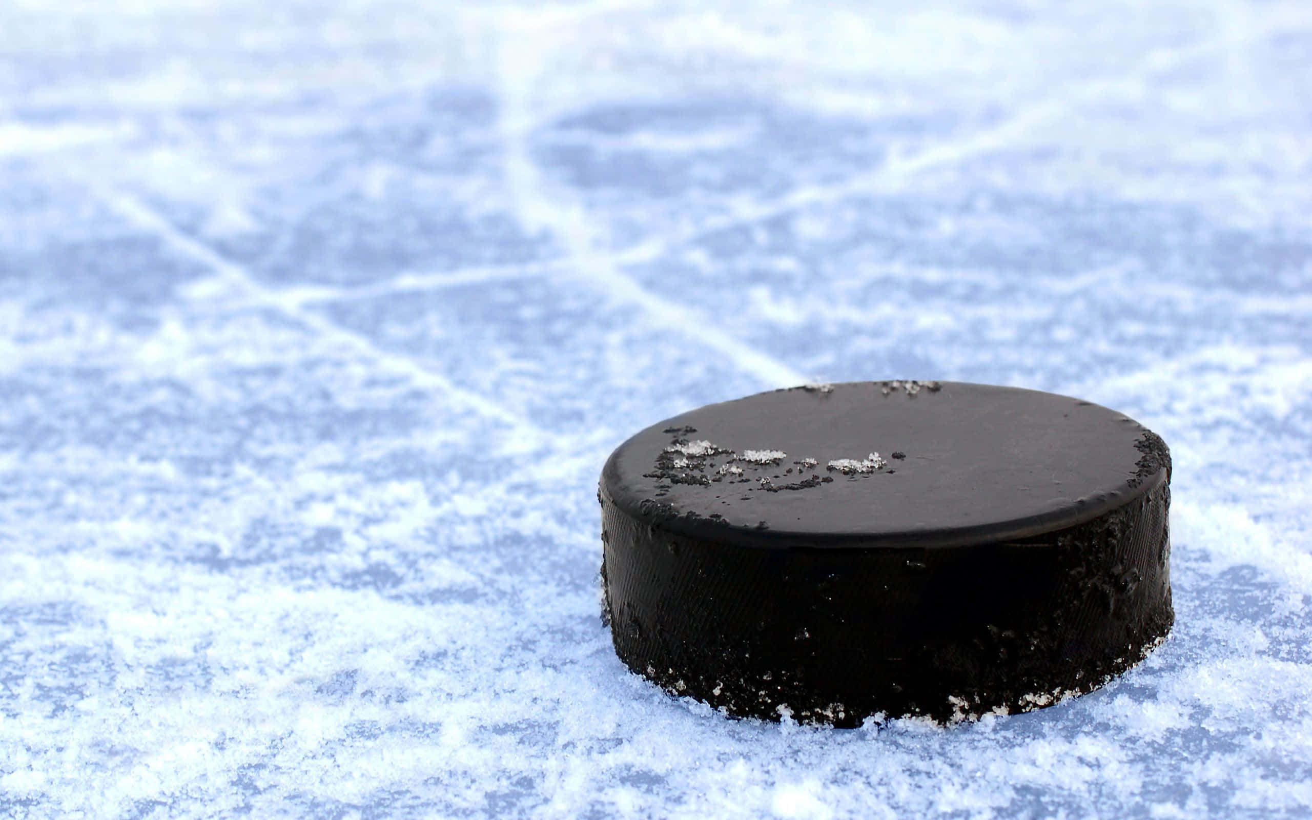 hockey 桌布 壁紙 — 一個黑色冰球放在有紋理的冰面上，邊緣附有霜晶，在明亮光線下。