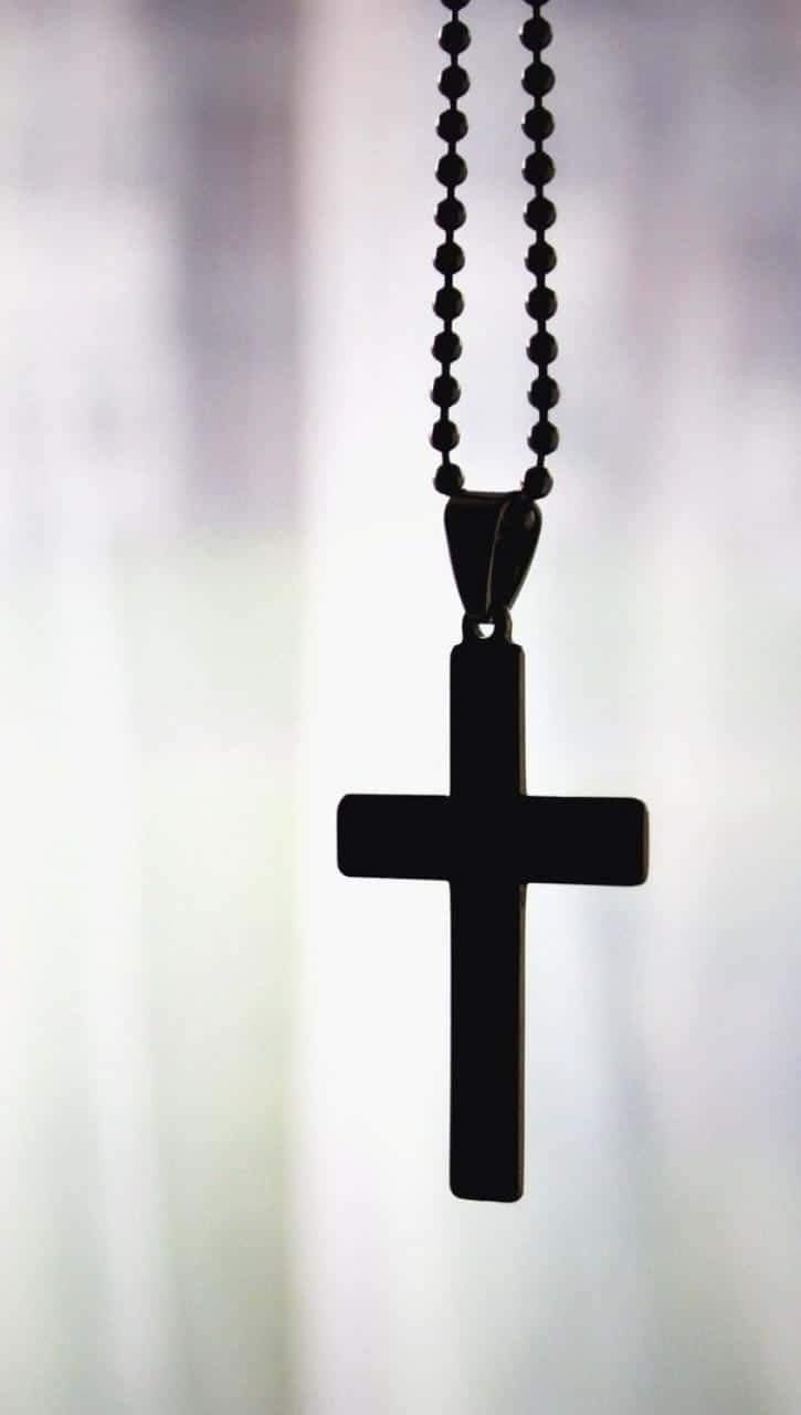 Cross Phone 桌布 壁紙 — 一個黑色十字架吊墜掛在珠鏈上，背景是柔和模糊的淺色。