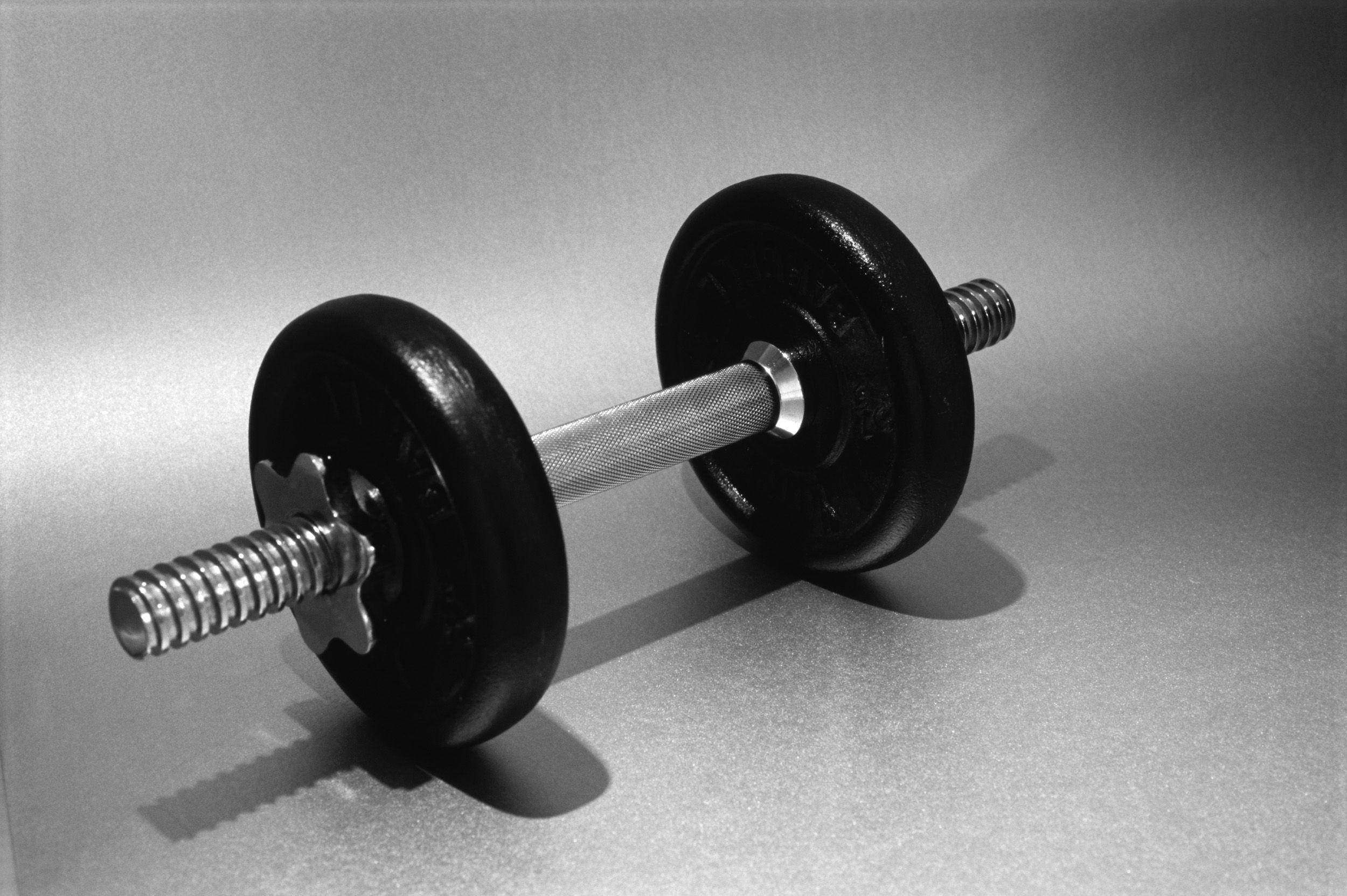 Barbell 桌布 壁紙 — 一個黑色和銀色的啞鈴在戲劇性的工作室燈光下對角線放置在一個中性灰色表面上。