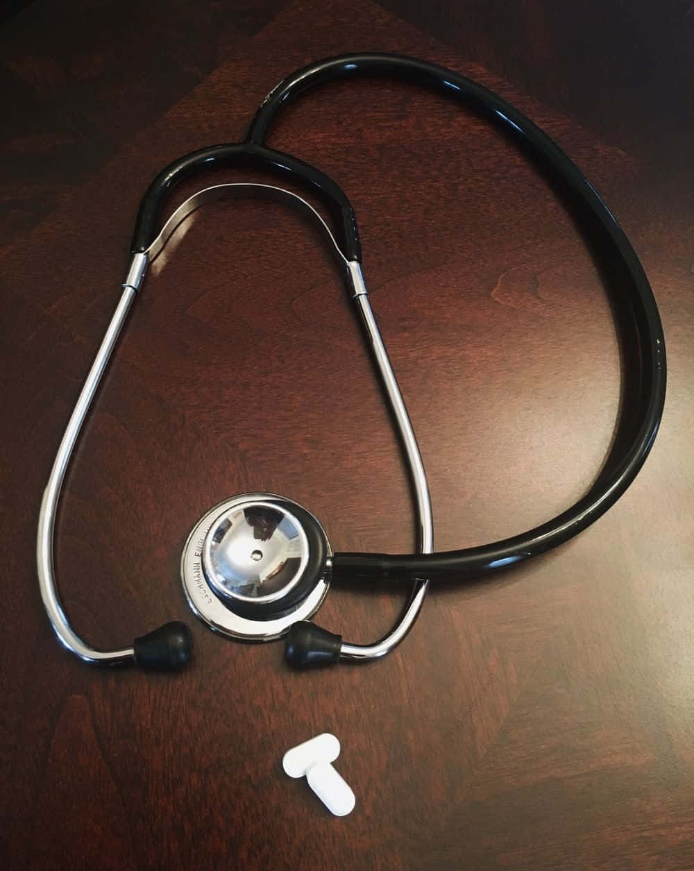 Stethoscope 桌布 壁紙 — 一個黑色和銀色的聽診器放在深色木質表面上，附近有白色耳塞。