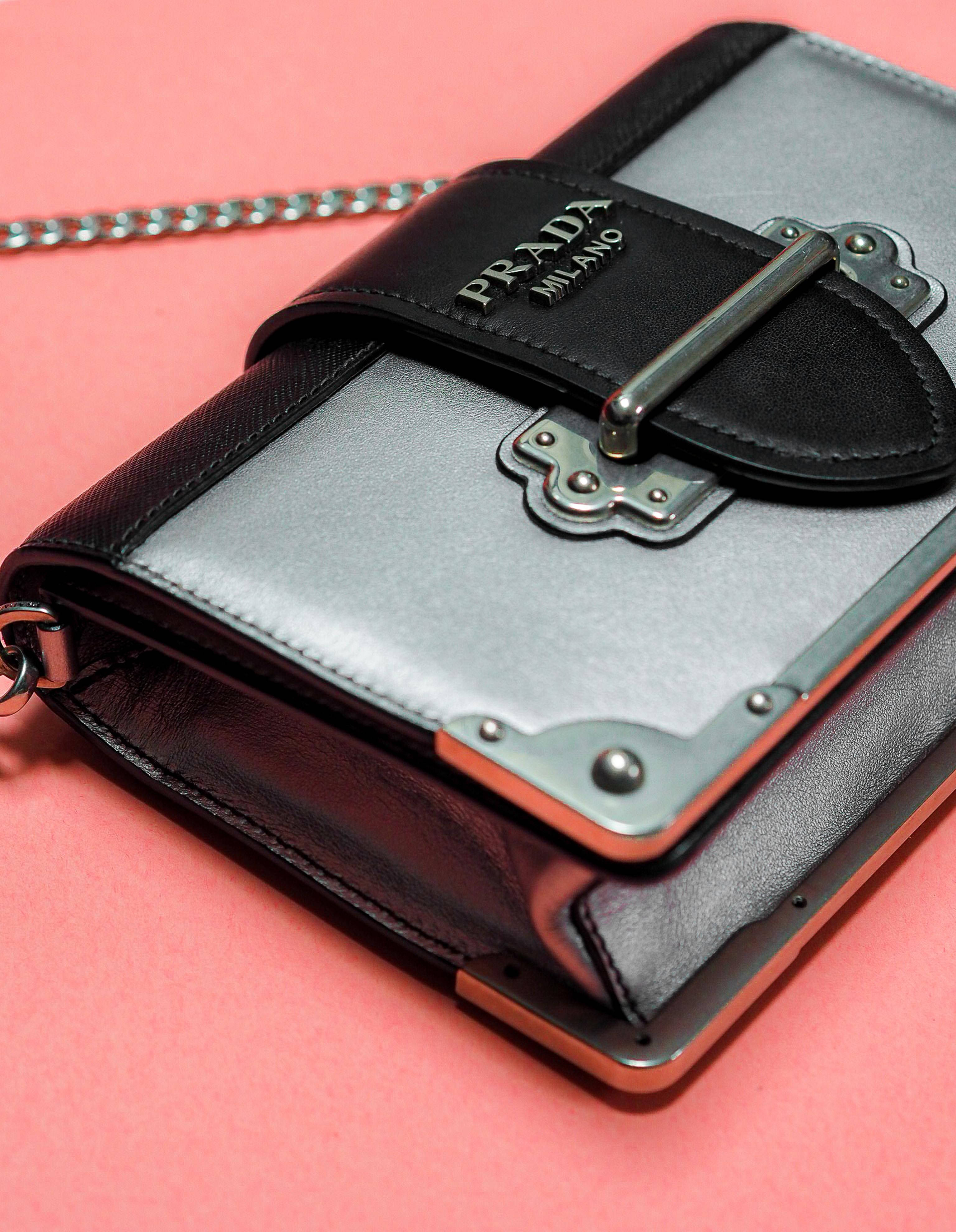 Prada 桌布 壁紙 — 一個黑色和銀色皮革及金屬配件的Prada手提包，放置在柔和的粉紅色背景上。