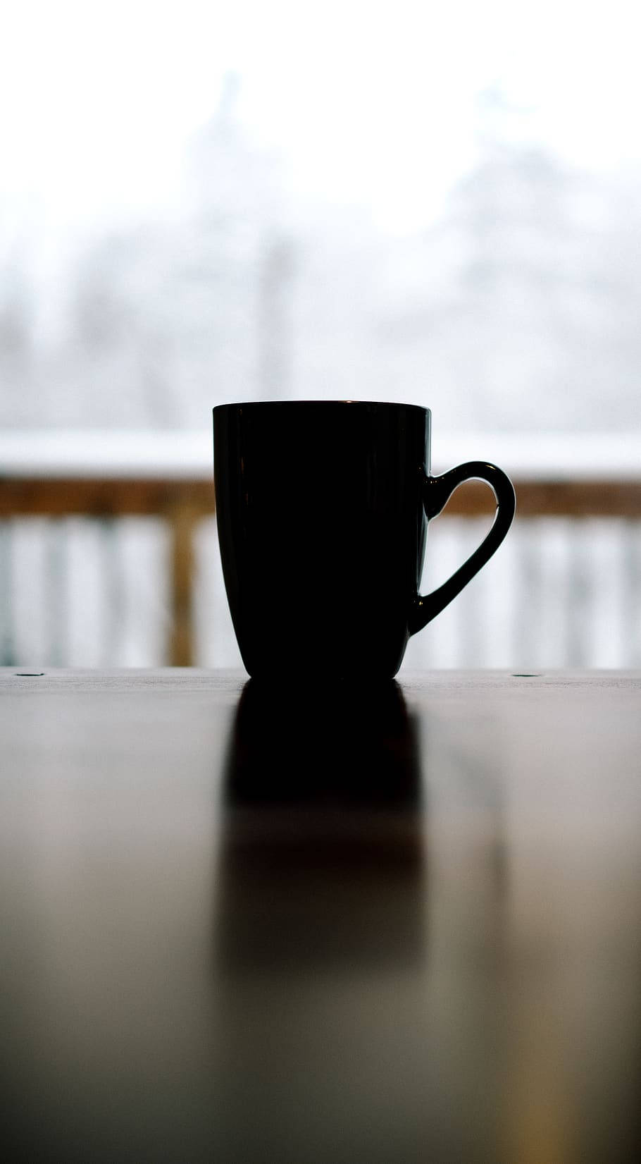 雪 桌布 壁紙 — 一個黑色咖啡杯放在木桌上，背景是模糊的雪景。