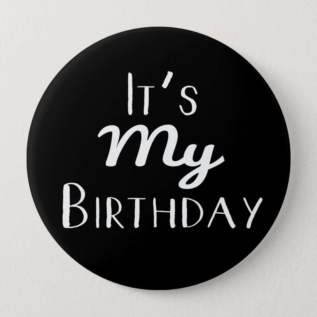 Birthday 桌布 壁紙 — 一個黑色圓形按鈕，上面有白色文字寫著「It's My Birthday」，字體混合，背景是素牆。