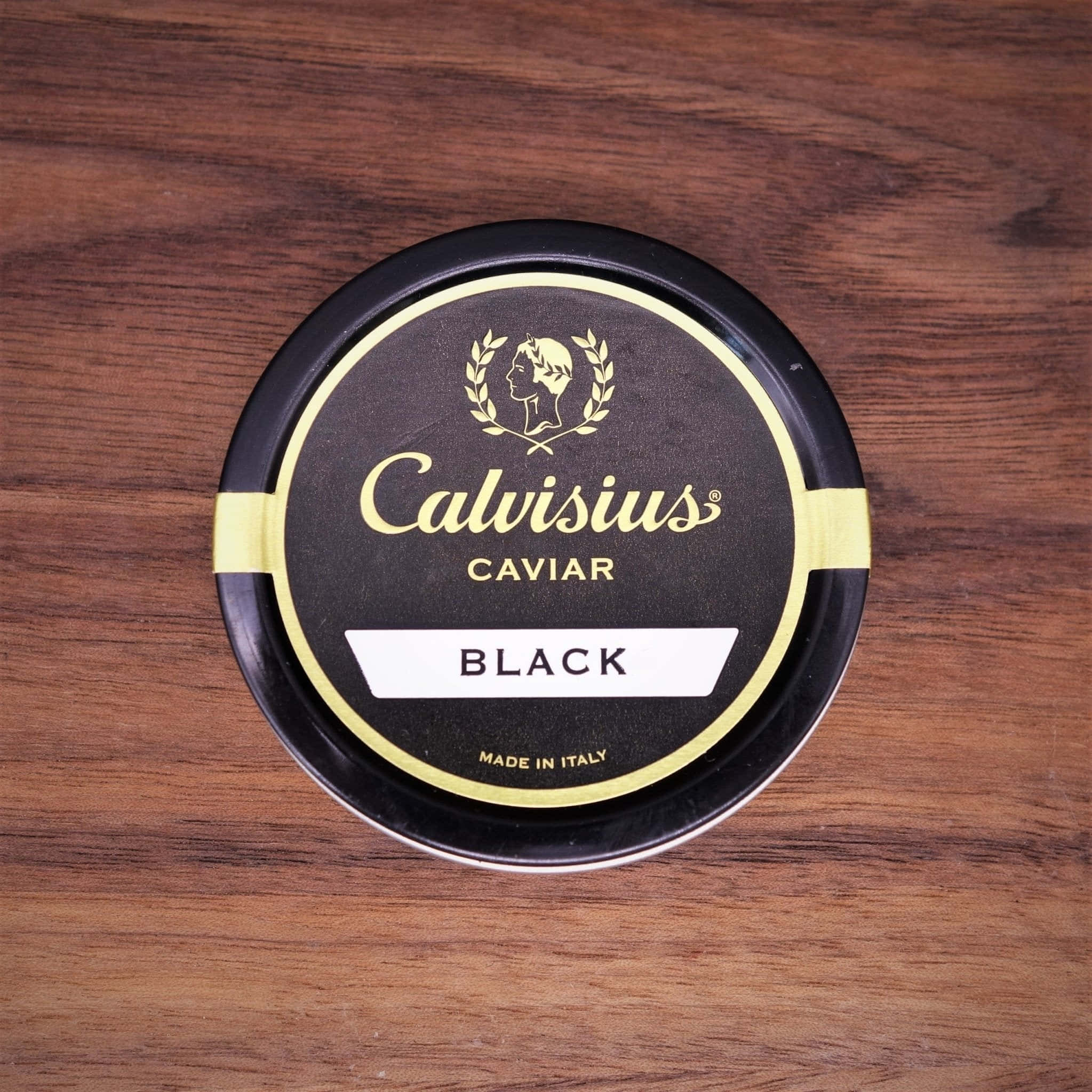 Black Caviar 桌布 壁紙 — 一個黑色圓形的Calvisius Caviar Black鞋油罐放在一塊豐富的棕色木質表面上。