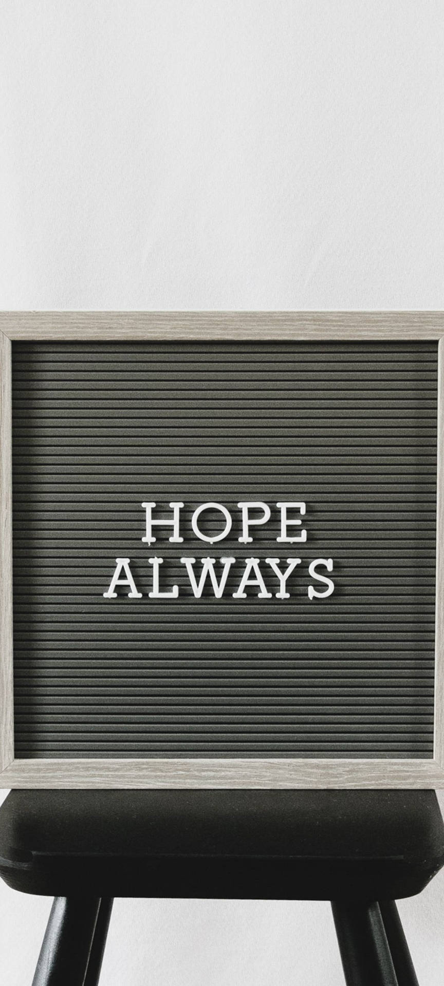 一個黑色字母板，上面用白色字母寫著HOPE ALWAYS，放在一個黑色凳子上。 — 勵志手機桌布 壁紙