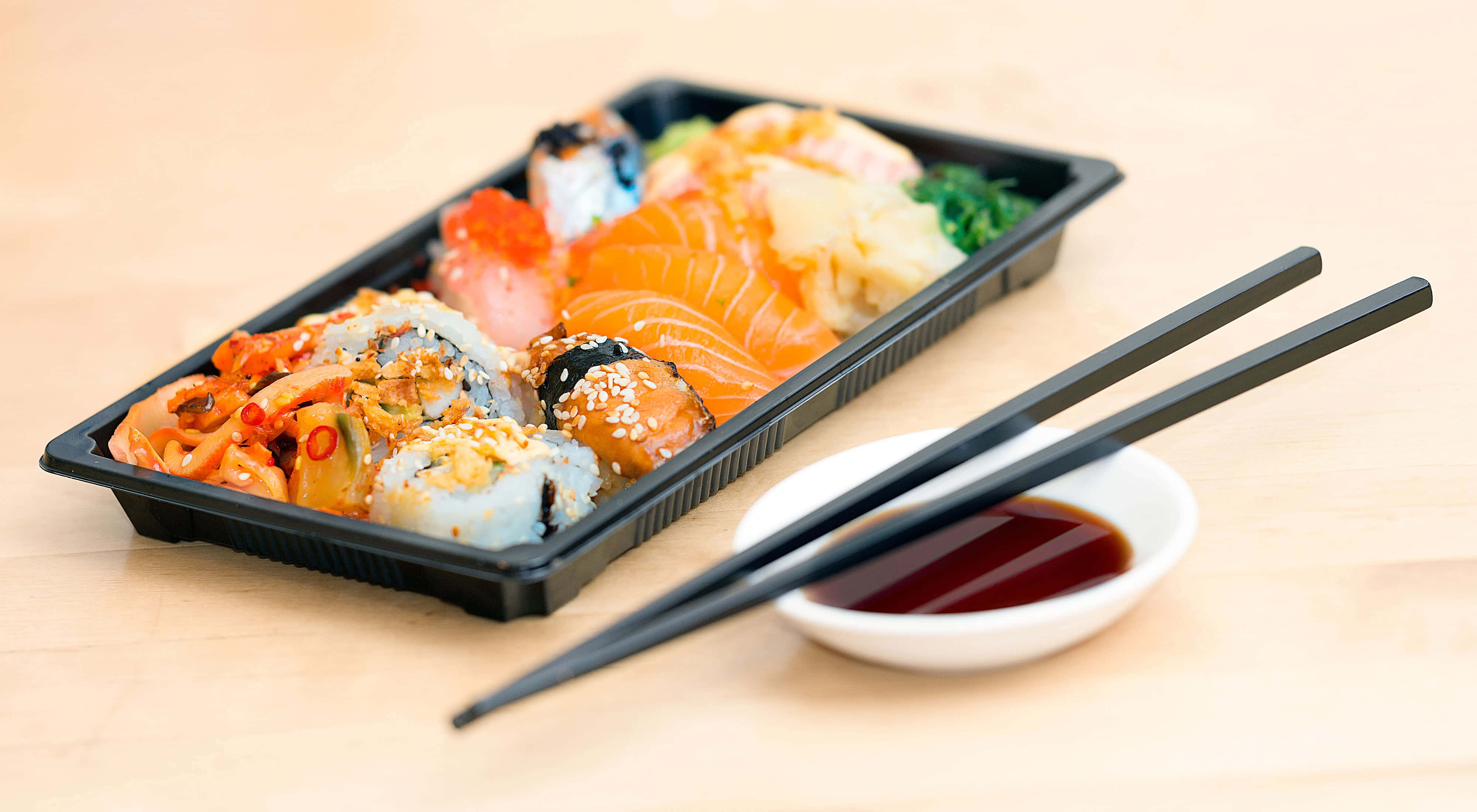 Food Photography 桌布 壁紙 — 一個黑色托盤上放有各種壽司卷和刺身，旁邊有一小碗醬油和黑色筷子，置於淺色木質表面上。