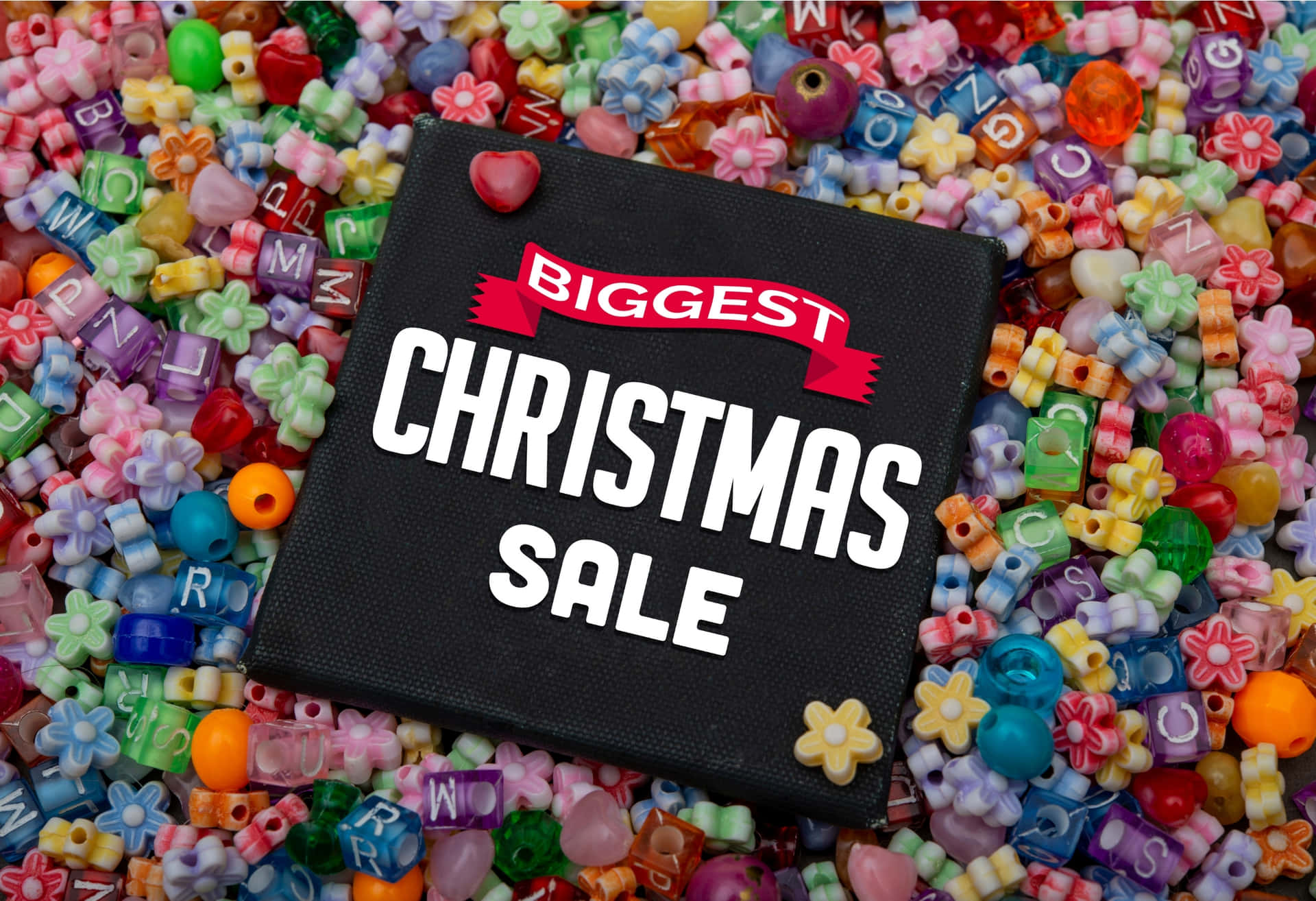 Biggest Christmas Sale Banner on Colorful Beads Background 壁紙 — 一個黑色標牌上寫著「BIGGEST CHRISTMAS SALE」，放在色彩繽紛的字母和花朵形狀珠子上。