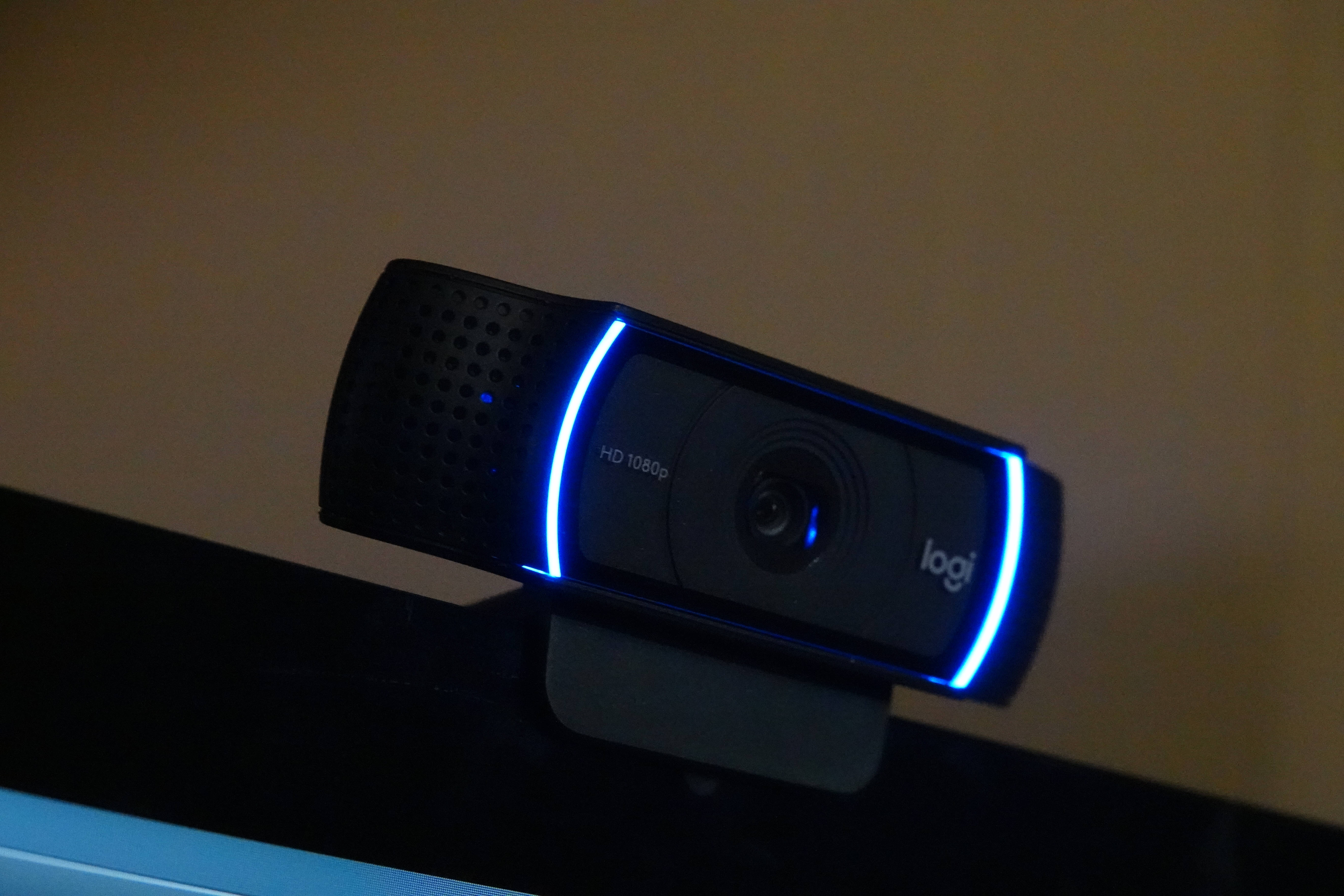 網路攝影機 桌布 壁紙 — 一個黑色的Logitech網路攝影機，帶有發光的藍色LED燈，在昏暗的燈光下放在顯示器上。