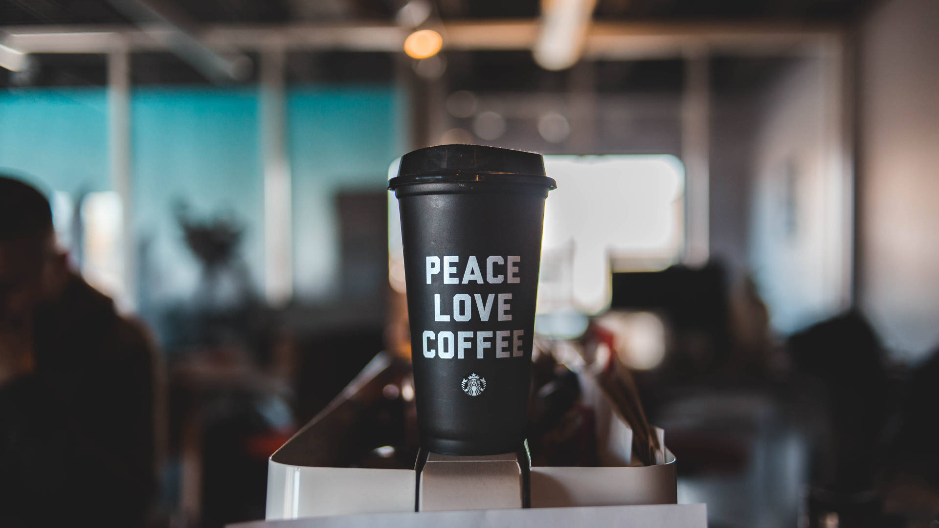 星巴克 桌布 壁紙 — 一個黑色的Starbucks咖啡杯，上面有白色的peace love coffee文字，聚焦在銀色托盤上，背景是柔和模糊的辦公室。