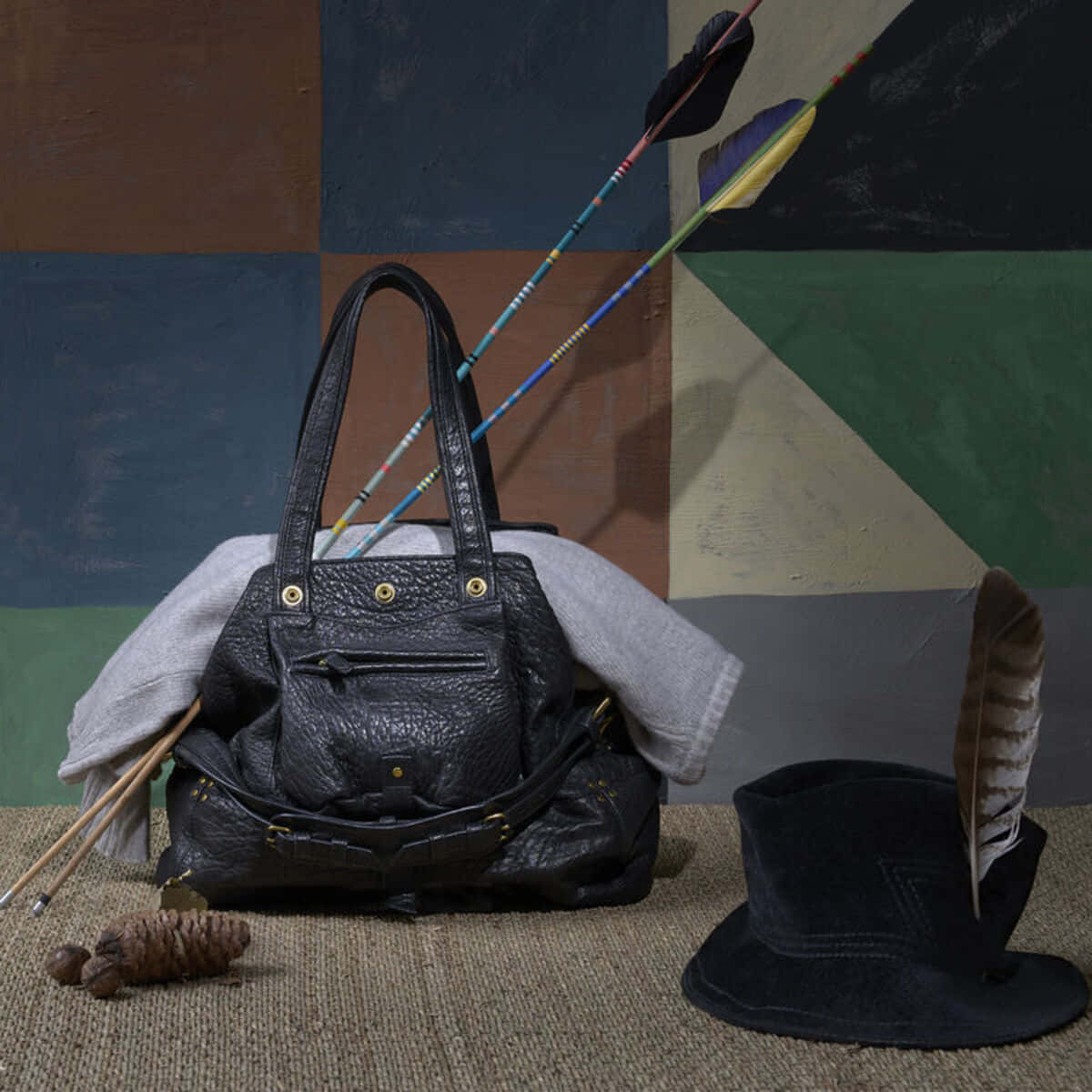 Handbag 桌布 壁紙 — 一個黑色皮革手提包放在一頂高帽和箭旁邊，背景是幾何圖案牆壁。