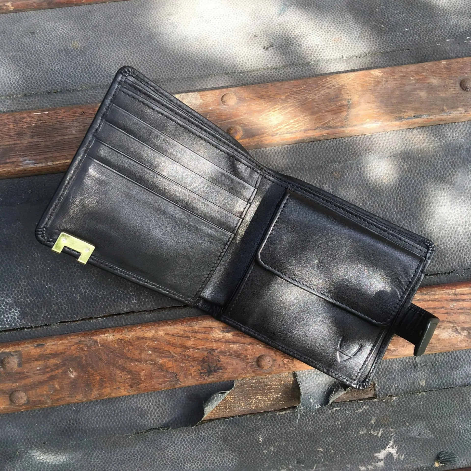 Black Leather 桌布 壁紙 — 一個黑色皮革錢包搭配金色拉鍊，在斑駁陽光下敞開放在風化的木長椅上。