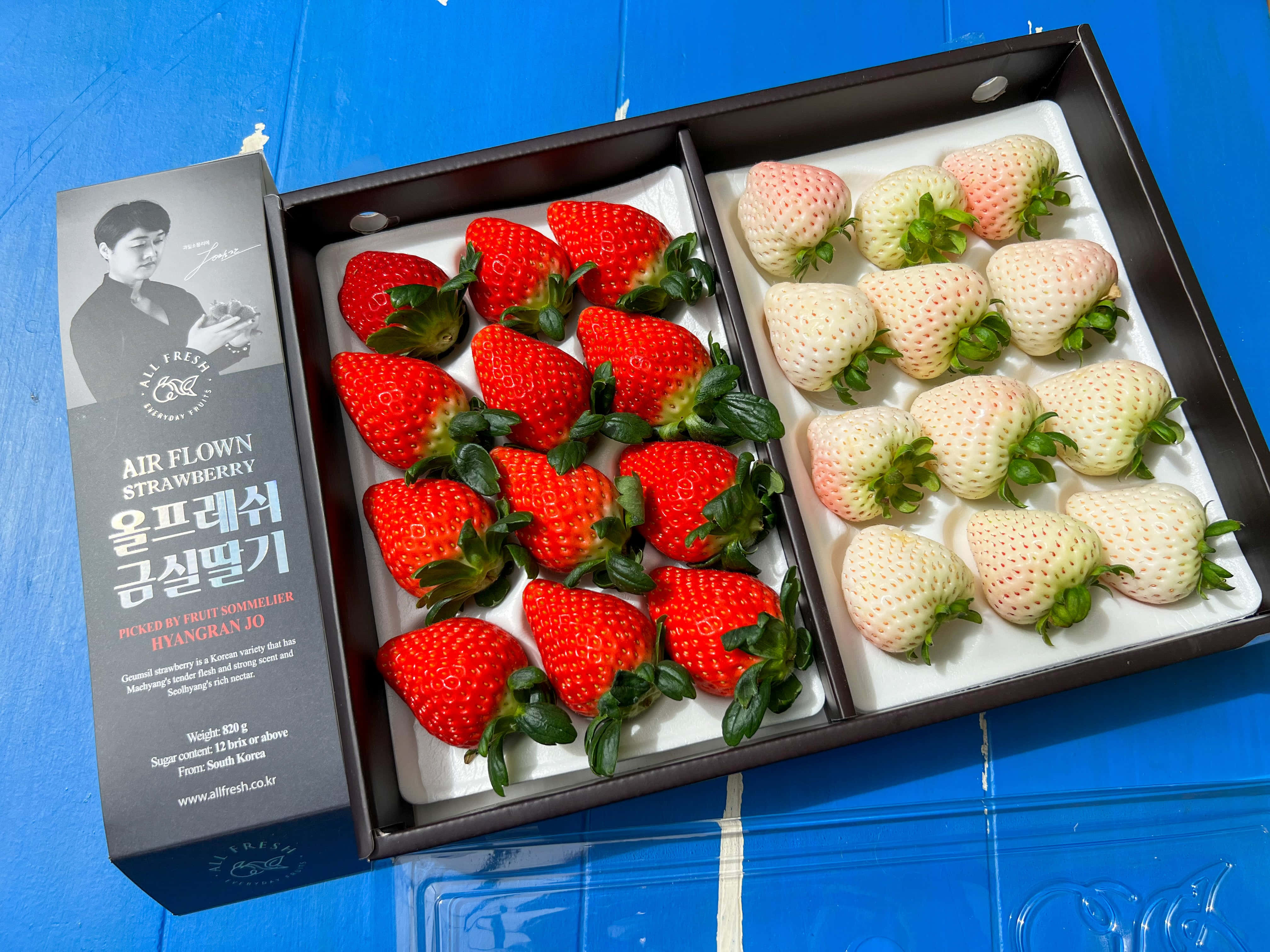Fruit 桌布 壁紙 — 一個黑色盒子展示鮮紅色和淡白色的草莓整齊地排列在白色泡沫上，背景是明亮的藍色。